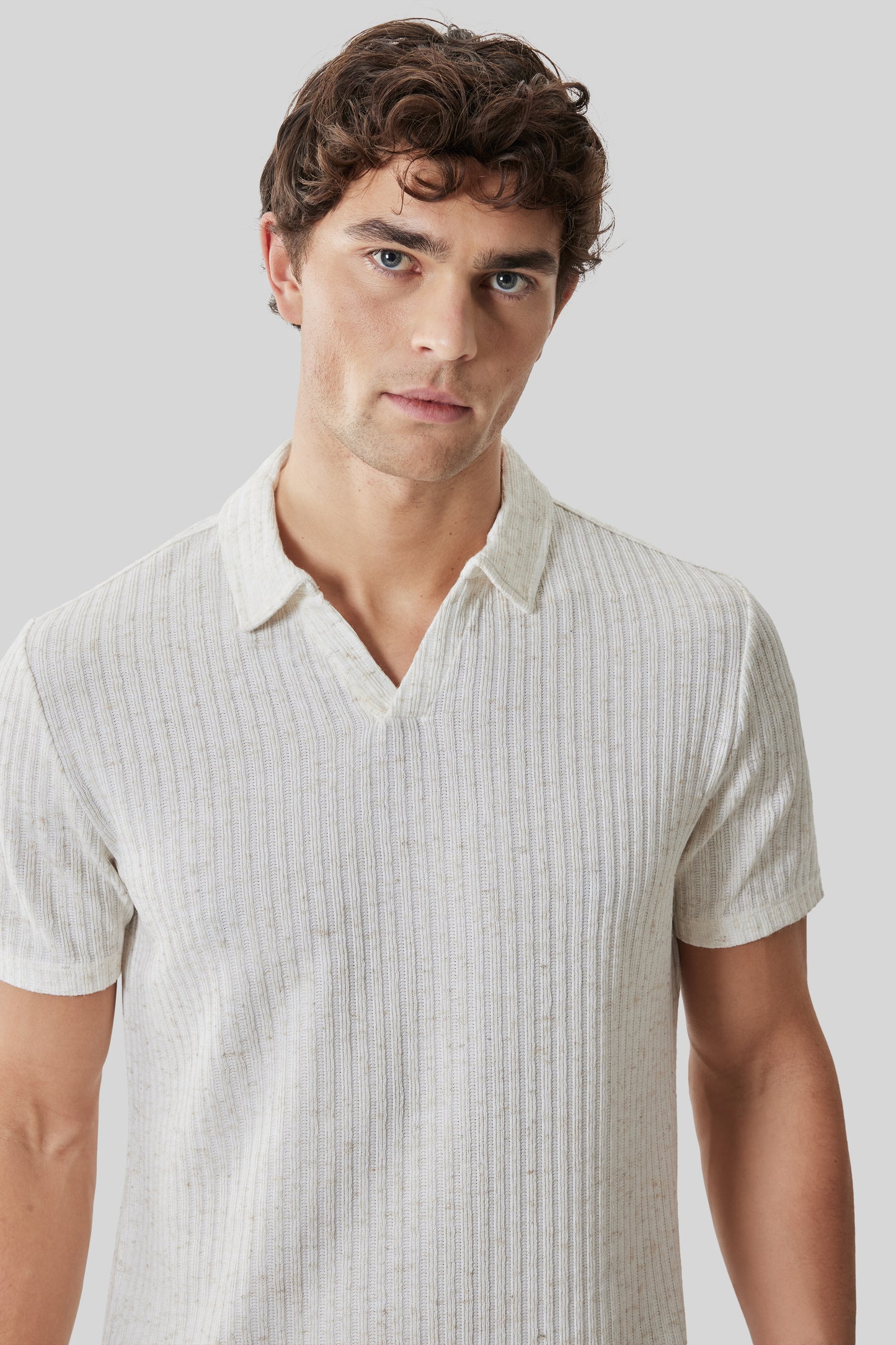 Beige ribbed short-sleeve polo shirt with open collar on male model against gray background.