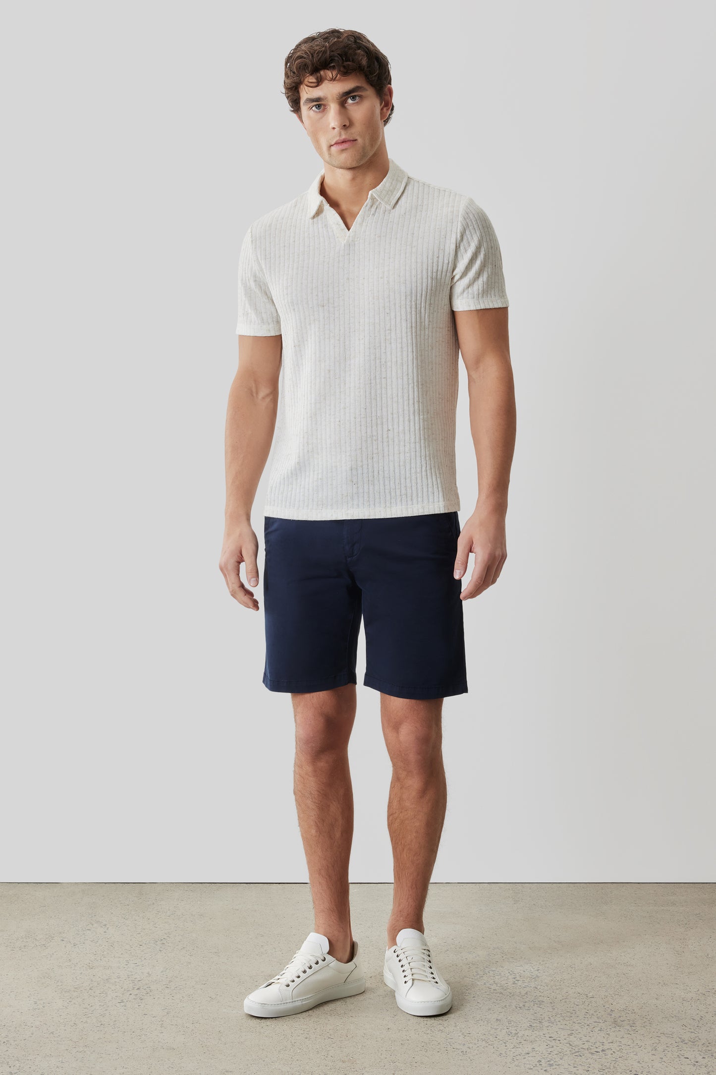 Man wearing cream ribbed short-sleeve polo shirt with open collar and navy shorts.