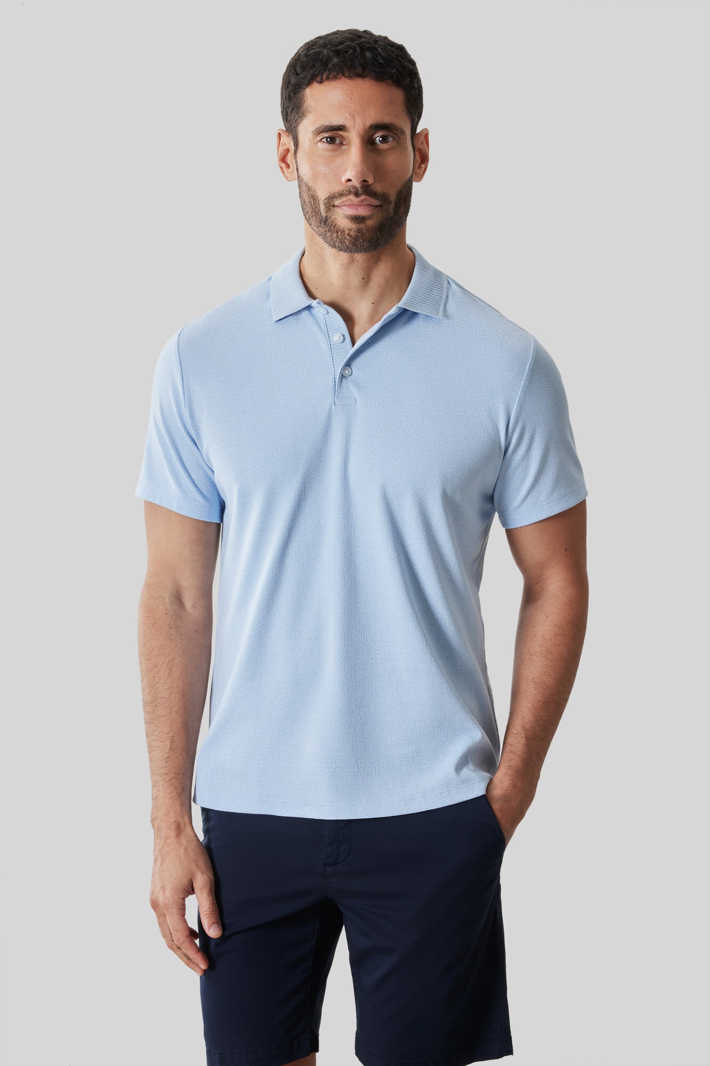 Man wearing light blue short-sleeve polo shirt with collar and button placket, paired with navy shorts.