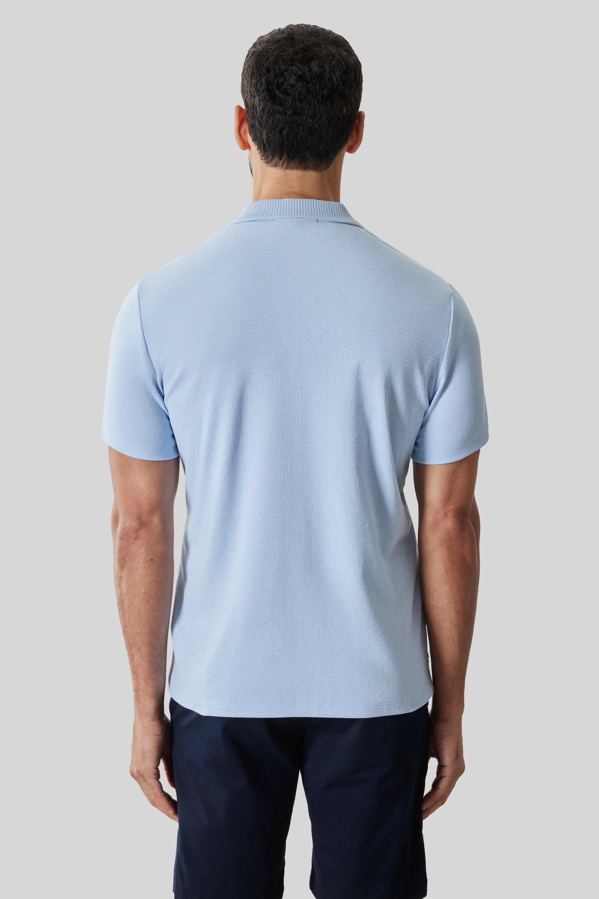 Light blue short sleeve polo shirt with ribbed collar, worn with dark navy pants.