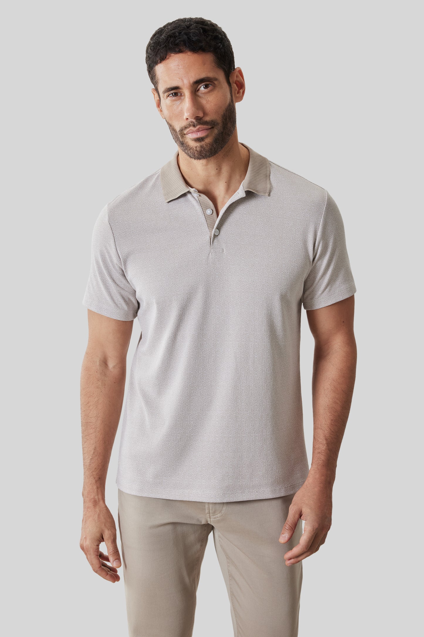Man wearing beige short-sleeve polo shirt with collar and button placket, paired with tan pants.