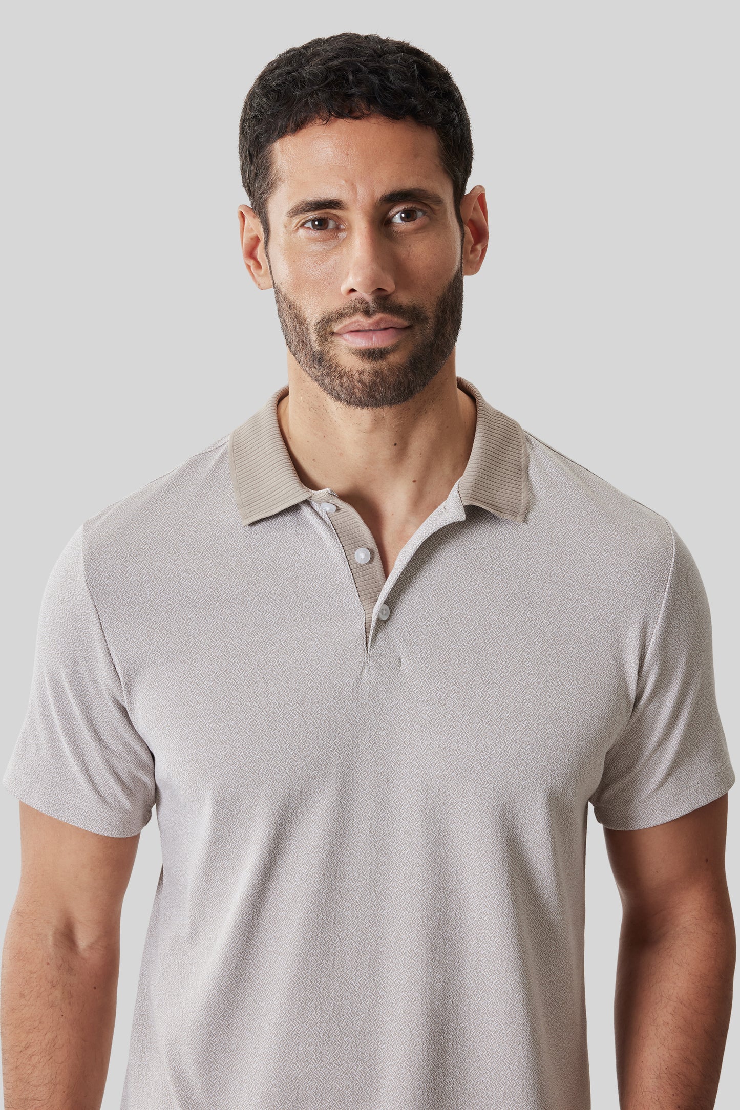 Beige short sleeve polo shirt with ribbed collar and button placket on male model.