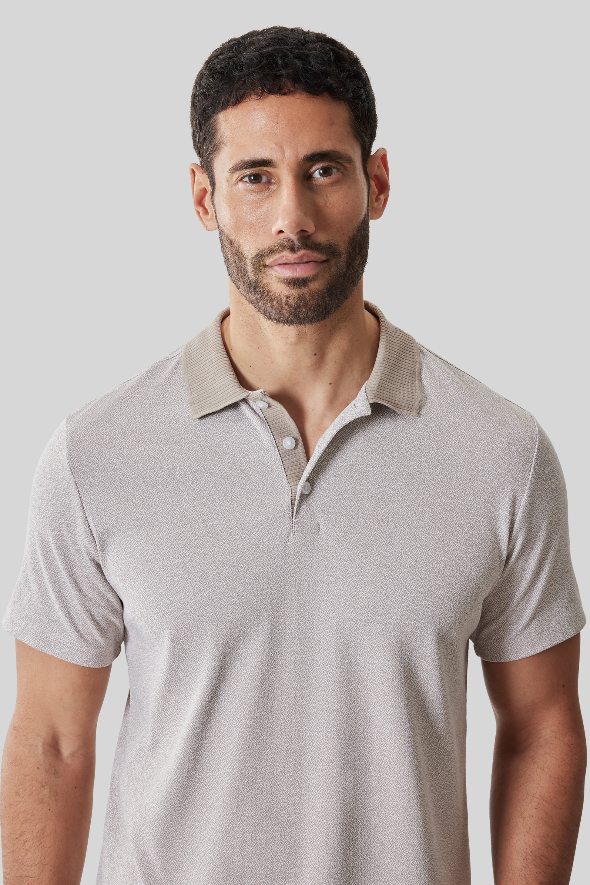 Beige short sleeve polo shirt with ribbed collar and button placket on male model.