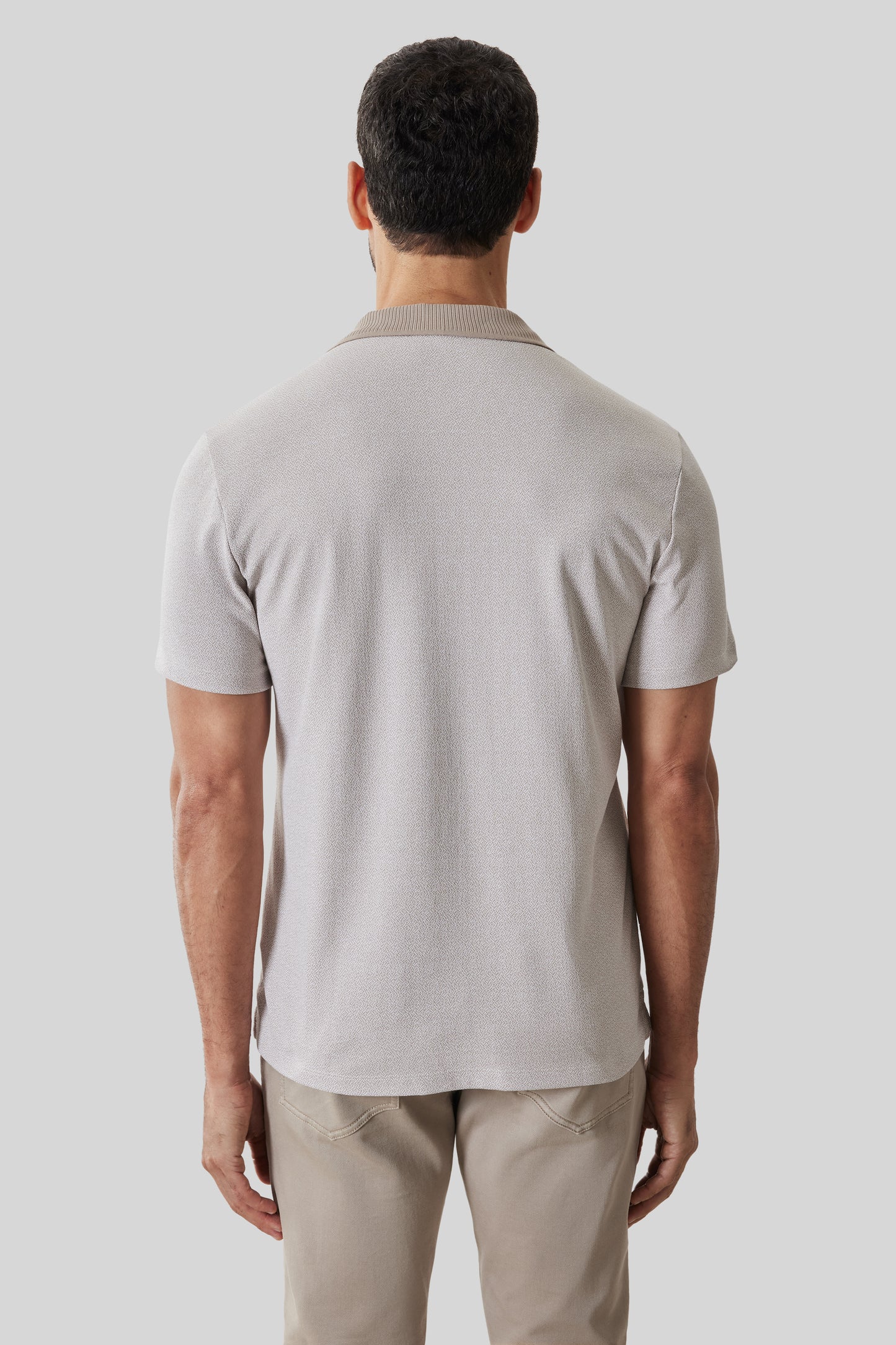 Man wearing light beige short-sleeve polo shirt with ribbed collar, shown from back view.