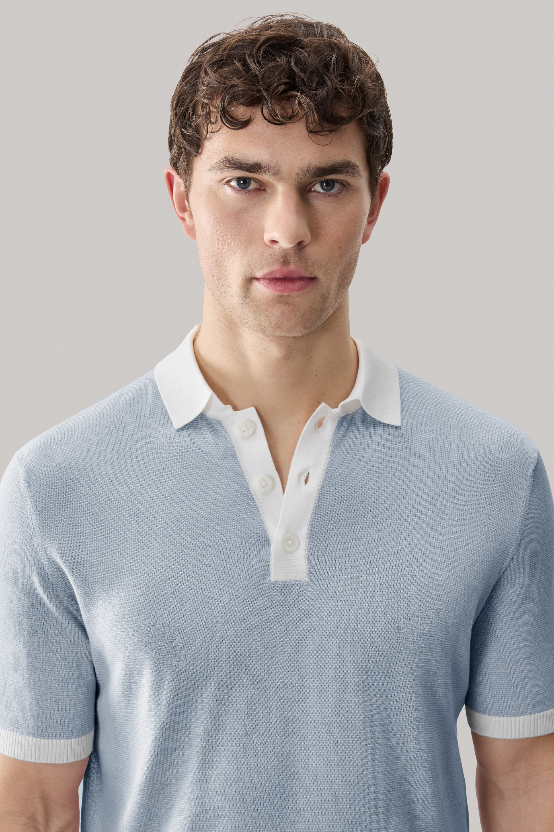 Man wearing light blue sweater polo with white collar and button placket.