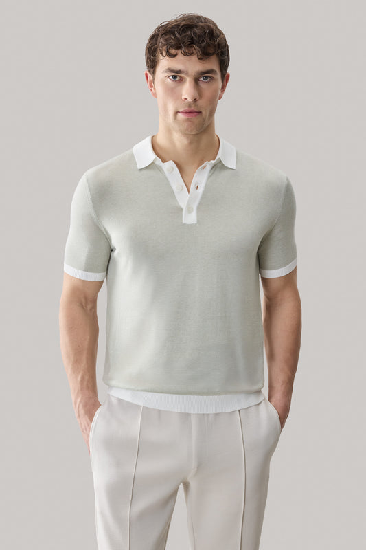 Man wearing sage green short-sleeve sweater polo with white collar and cuff trim over cream pants.