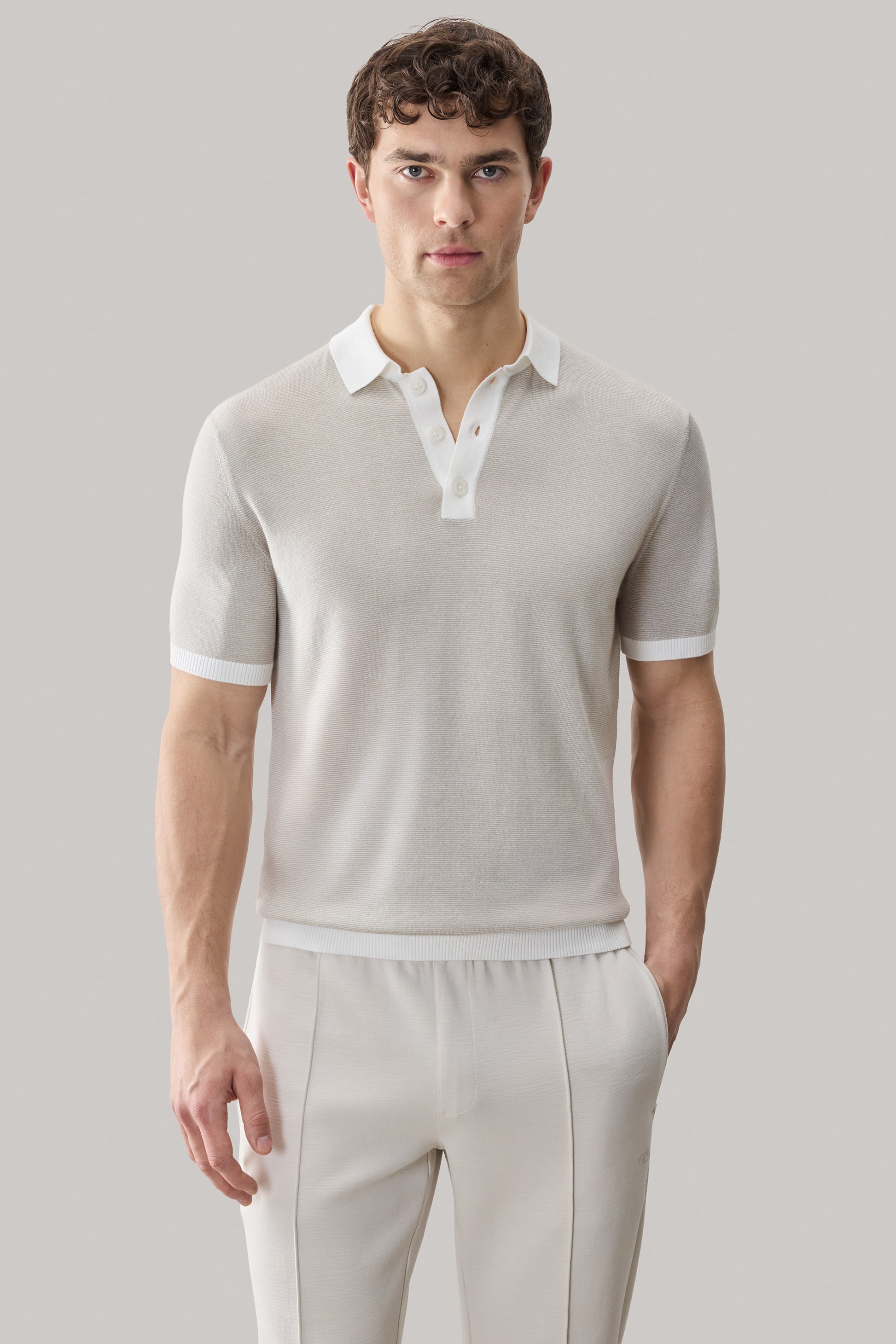 Beige sweater polo with white collar and trim, short sleeves with ribbed cuffs.