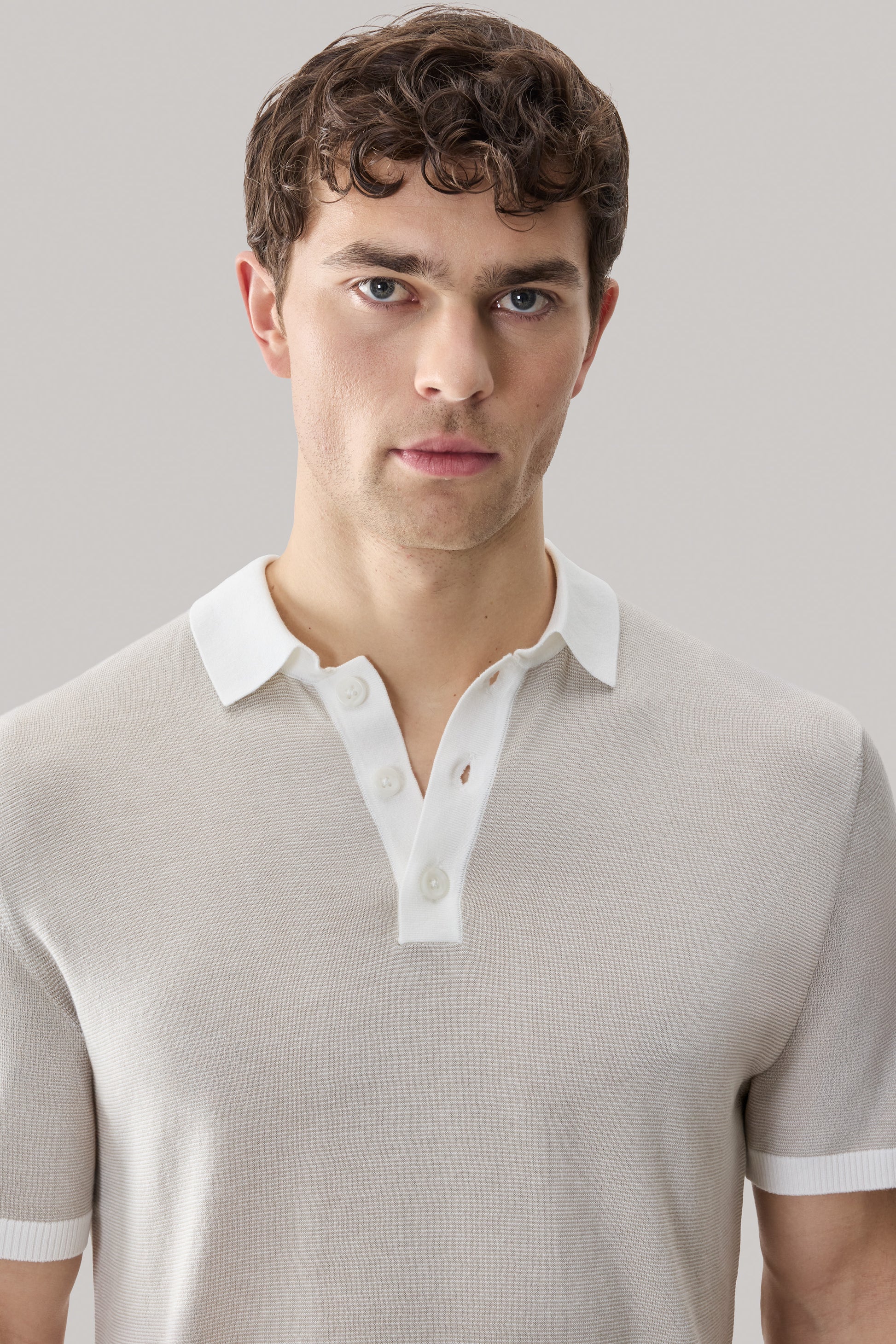 Man wearing beige sweater polo with white collar and button placket.