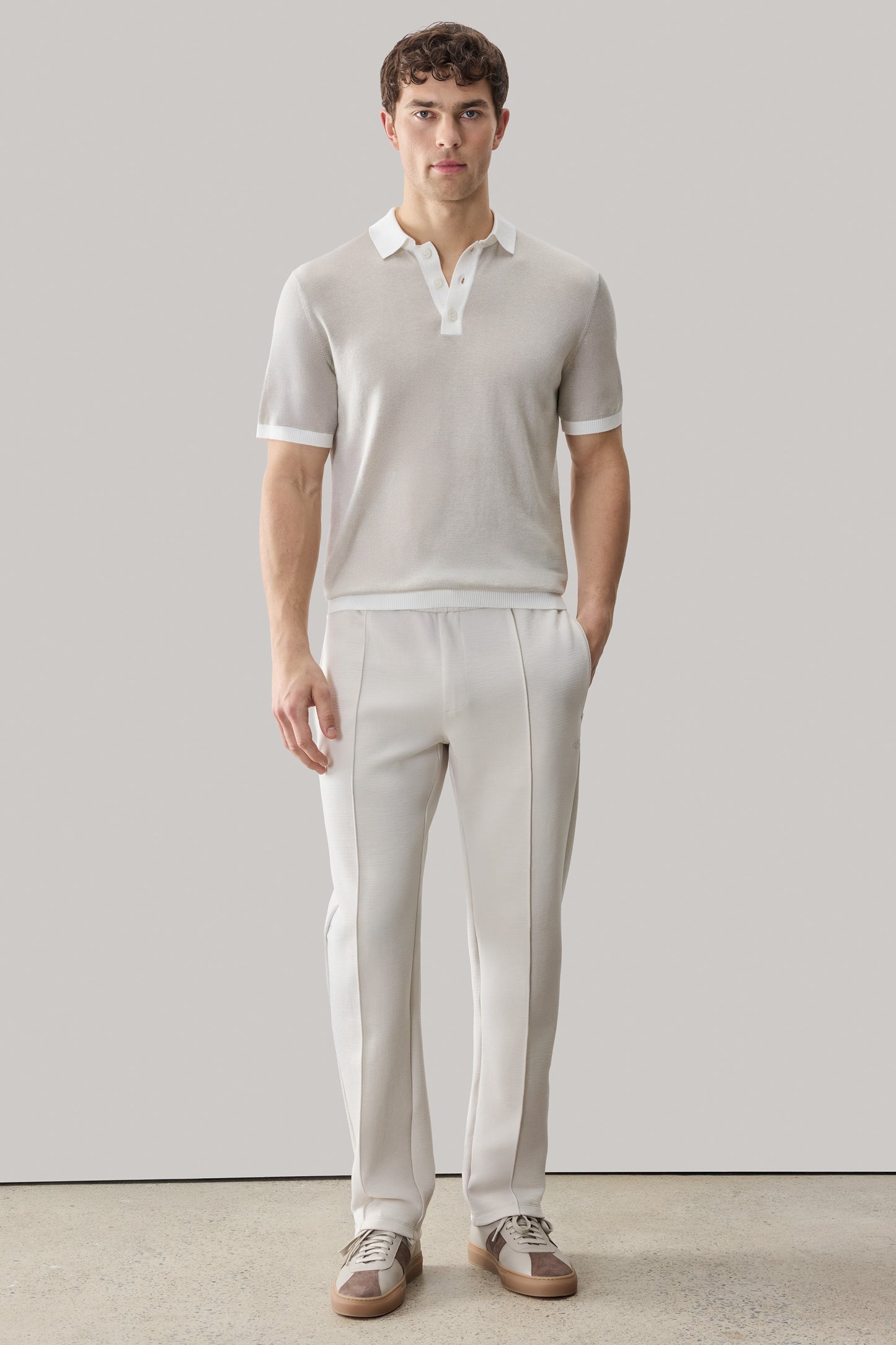 Man wearing cream polo shirt with white collar and trim, paired with cream trousers and two-tone sneakers.