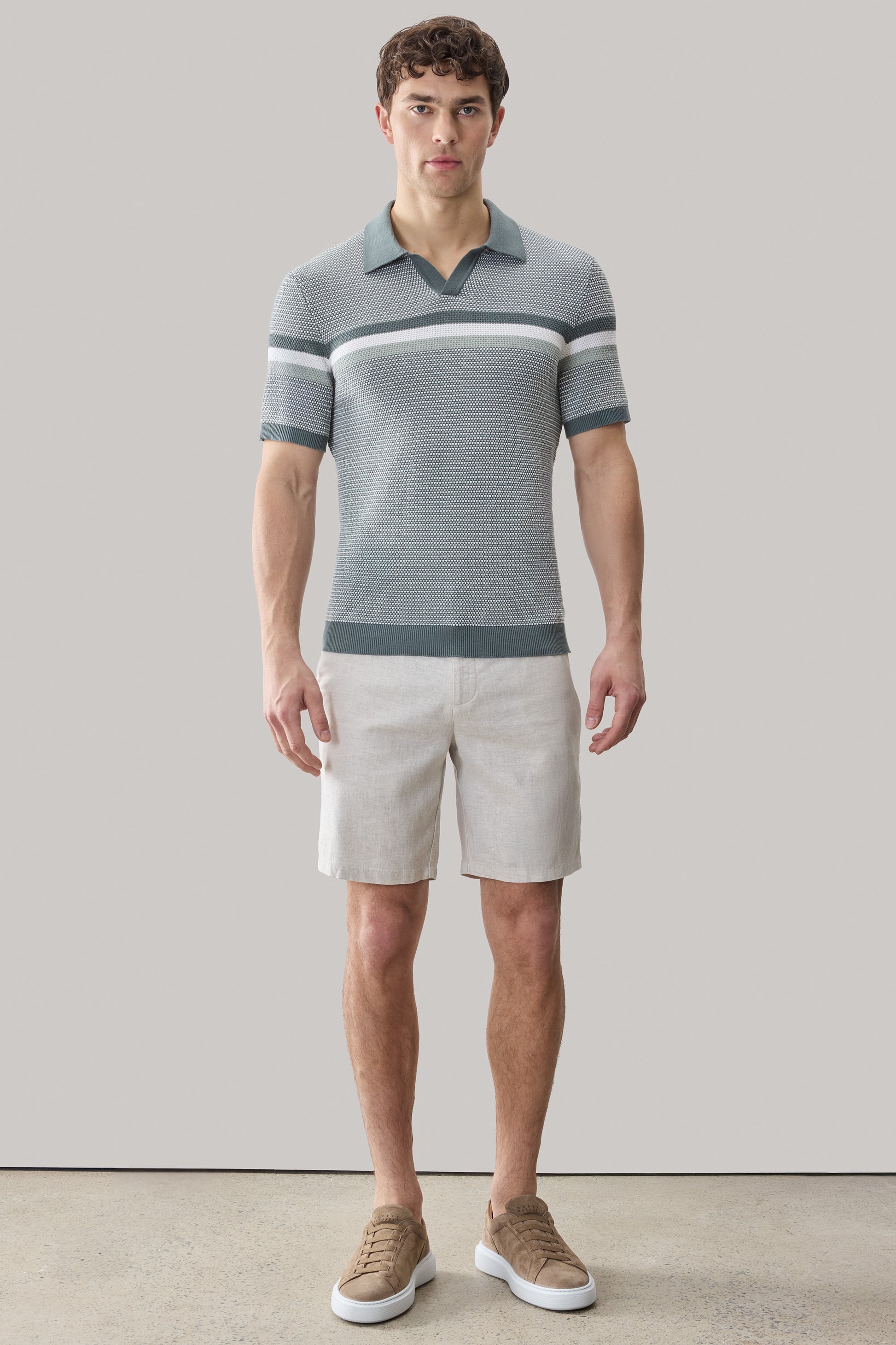 Man wearing gray striped short-sleeve polo sweater with open collar and white shorts.