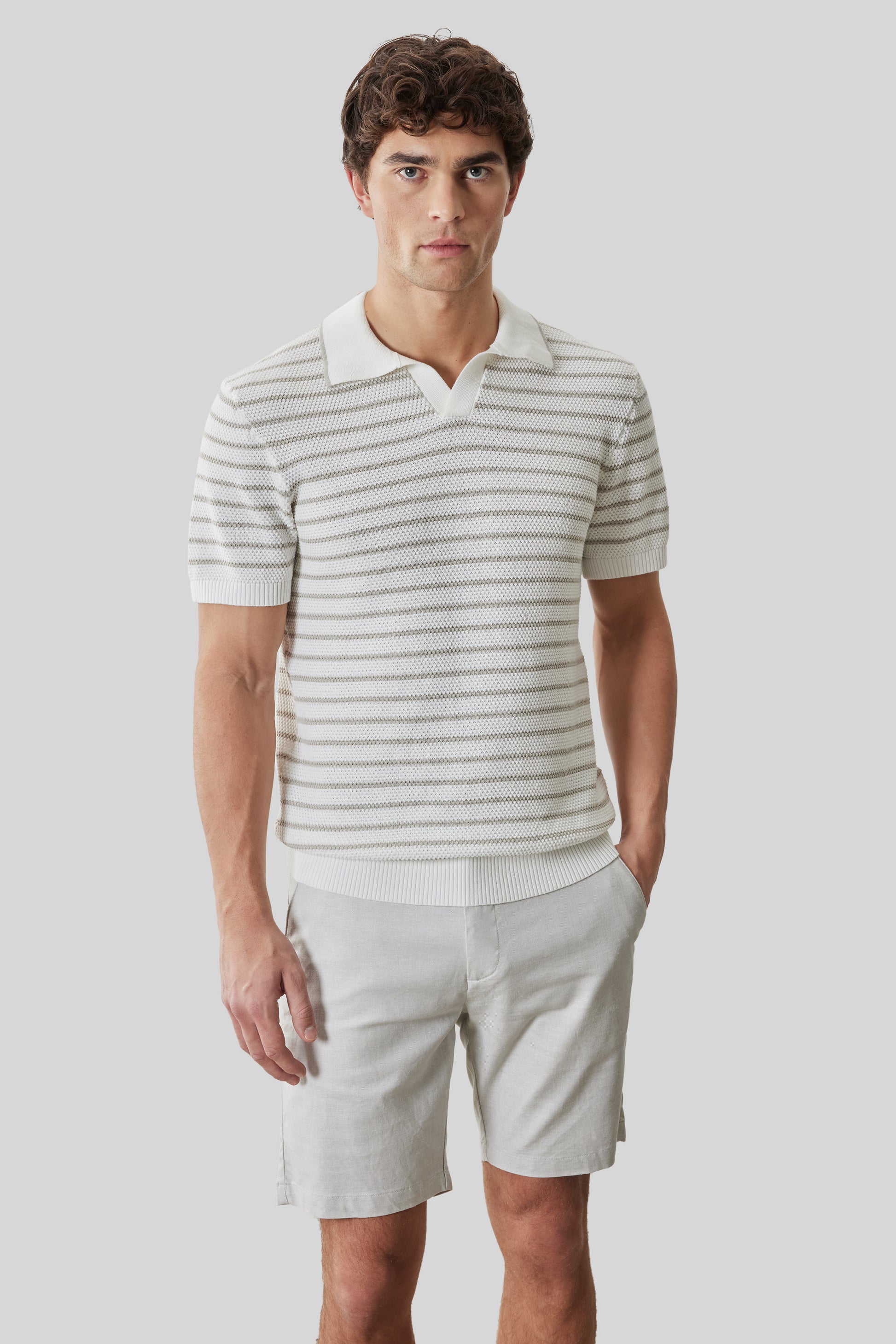 Striped short-sleeve polo with open collar in cream and gray worn with cream shorts.