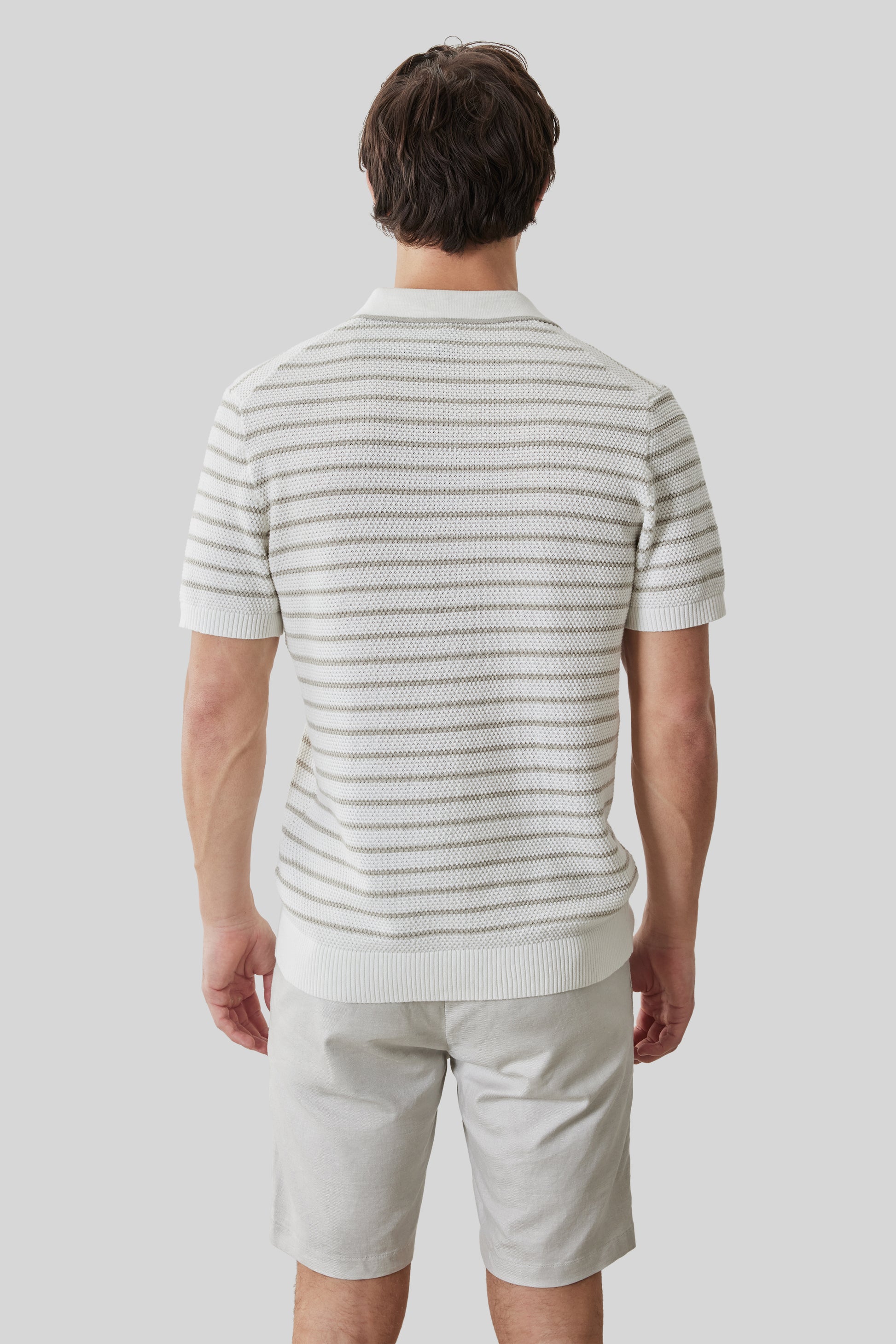 Man wearing cream and gray striped open collar polo shirt with short sleeves, paired with light khaki shorts.
