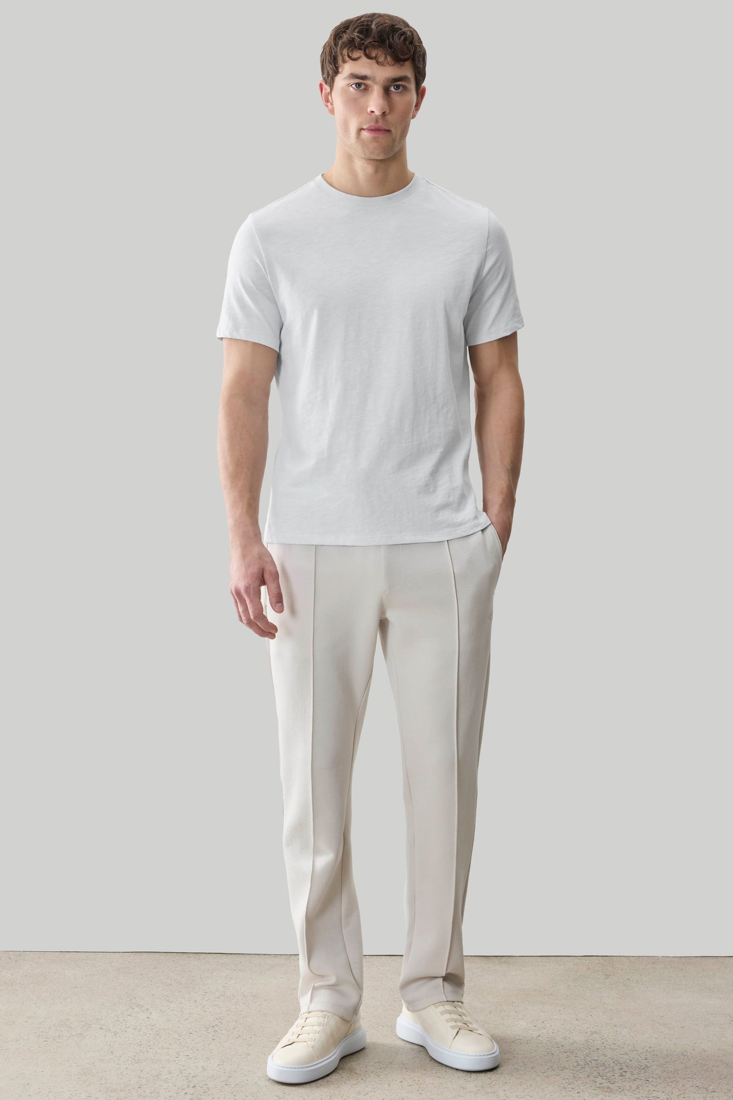 Man wearing light gray short-sleeve crew neck tee with cream pants and white sneakers.