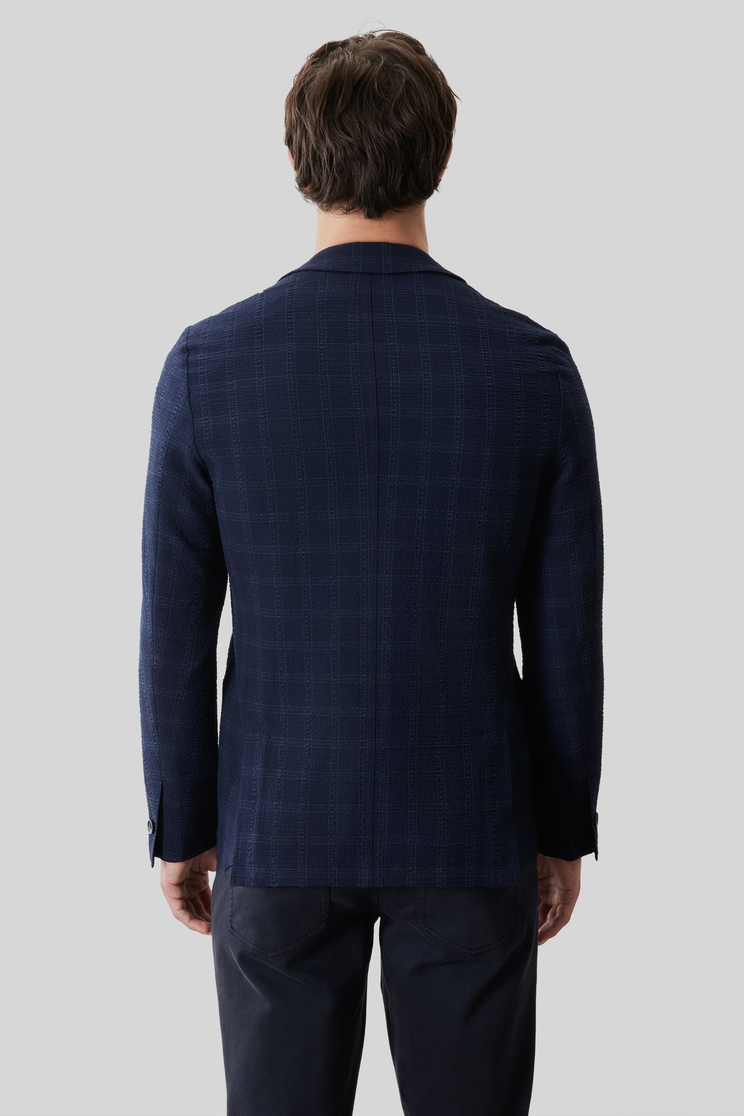 Man wearing navy blue checked sportcoat with long sleeves, shown from back view.