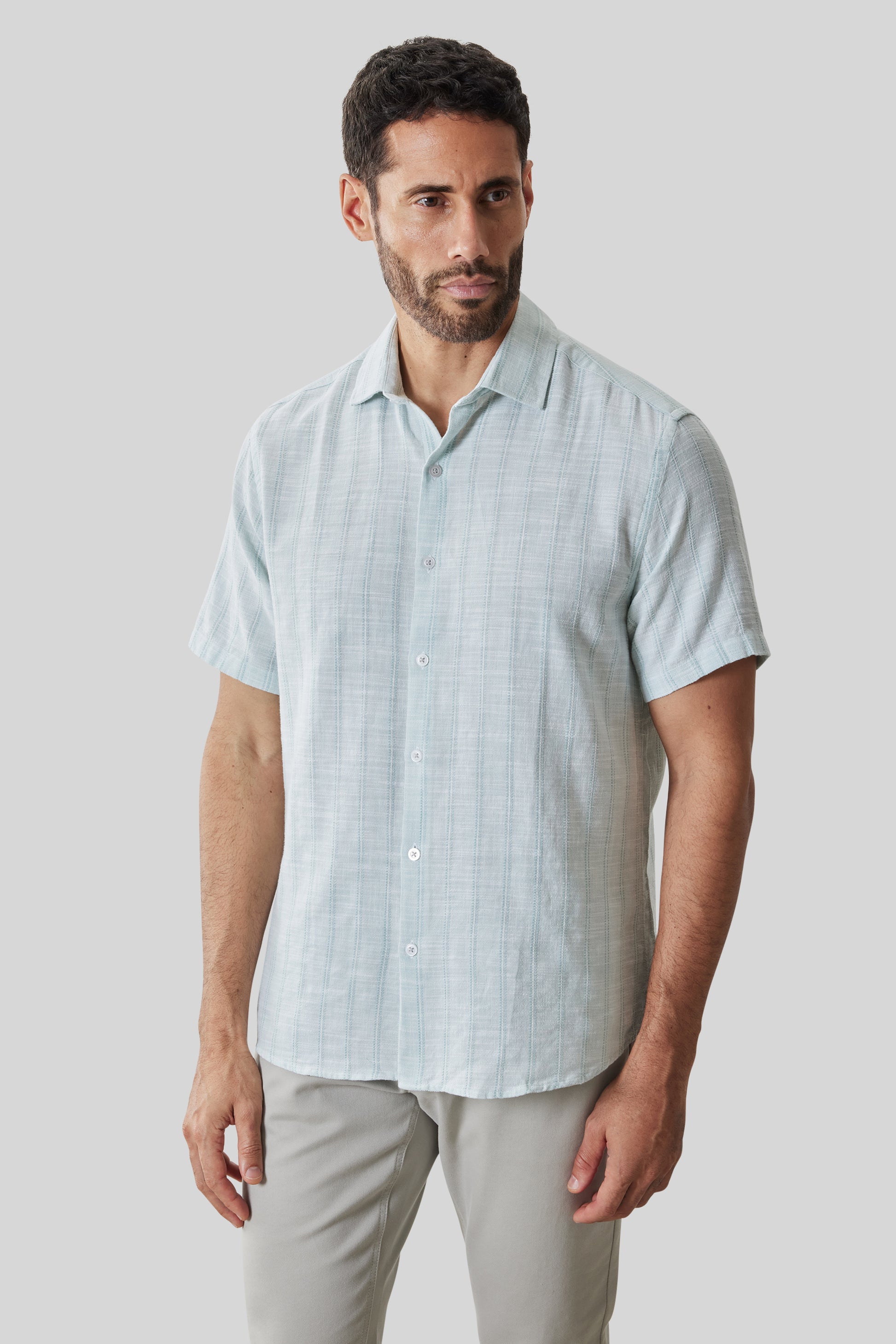 Light blue plaid short sleeve button-up shirt with white buttons, displayed on a model wearing beige pants.