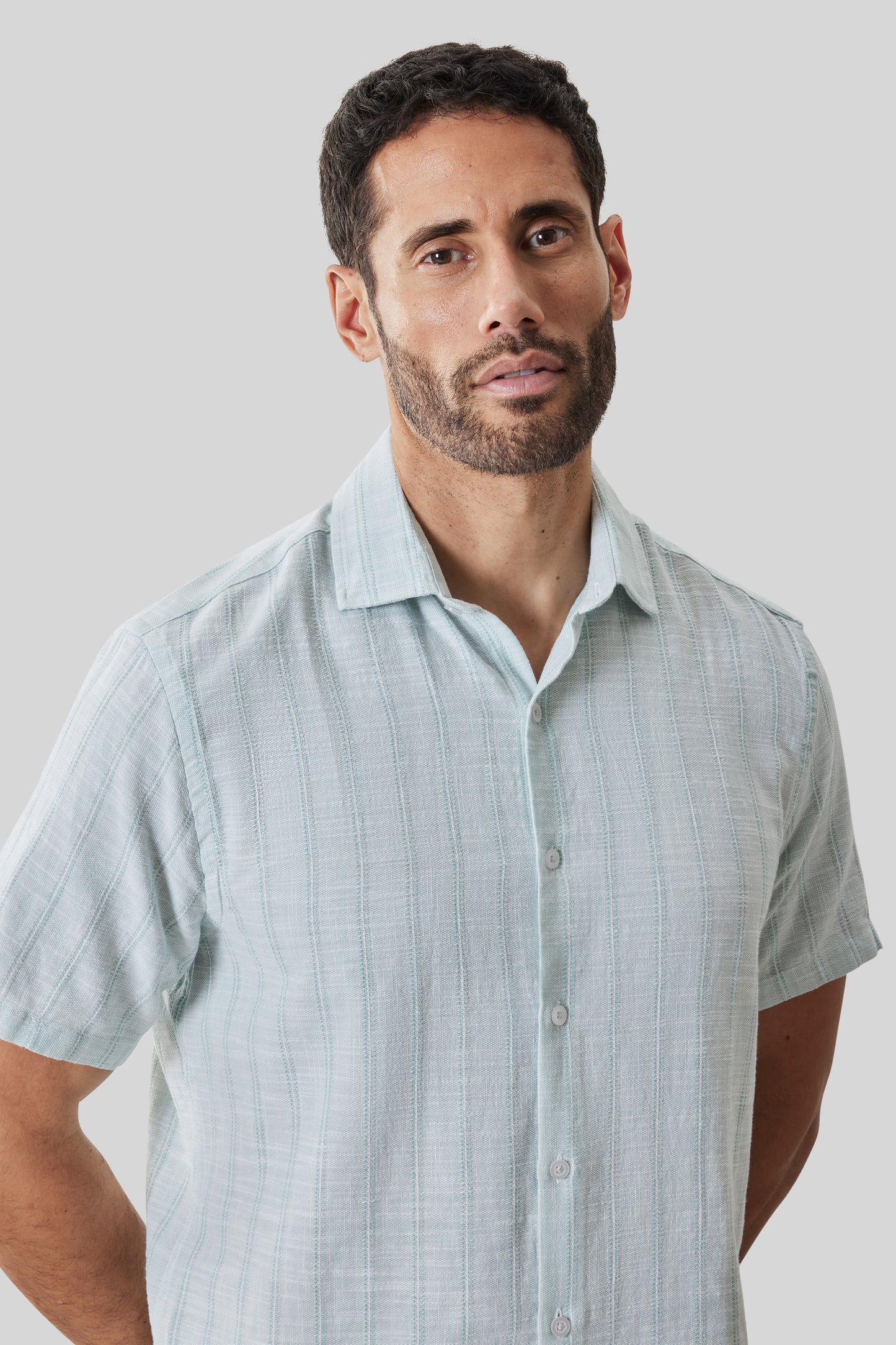 Light blue striped short sleeve button-up shirt with collar, displayed on a man against neutral background.