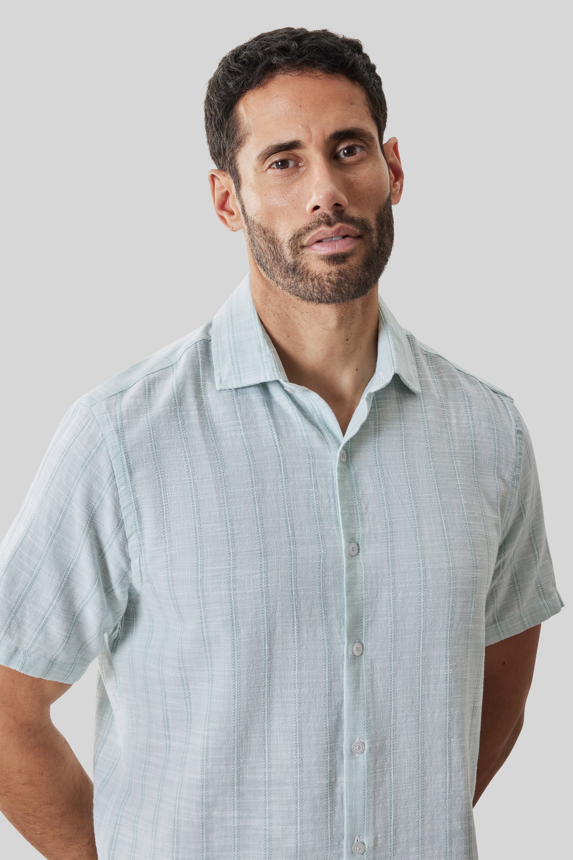 Light blue striped short sleeve button-up shirt with collar, displayed on a man against neutral background.