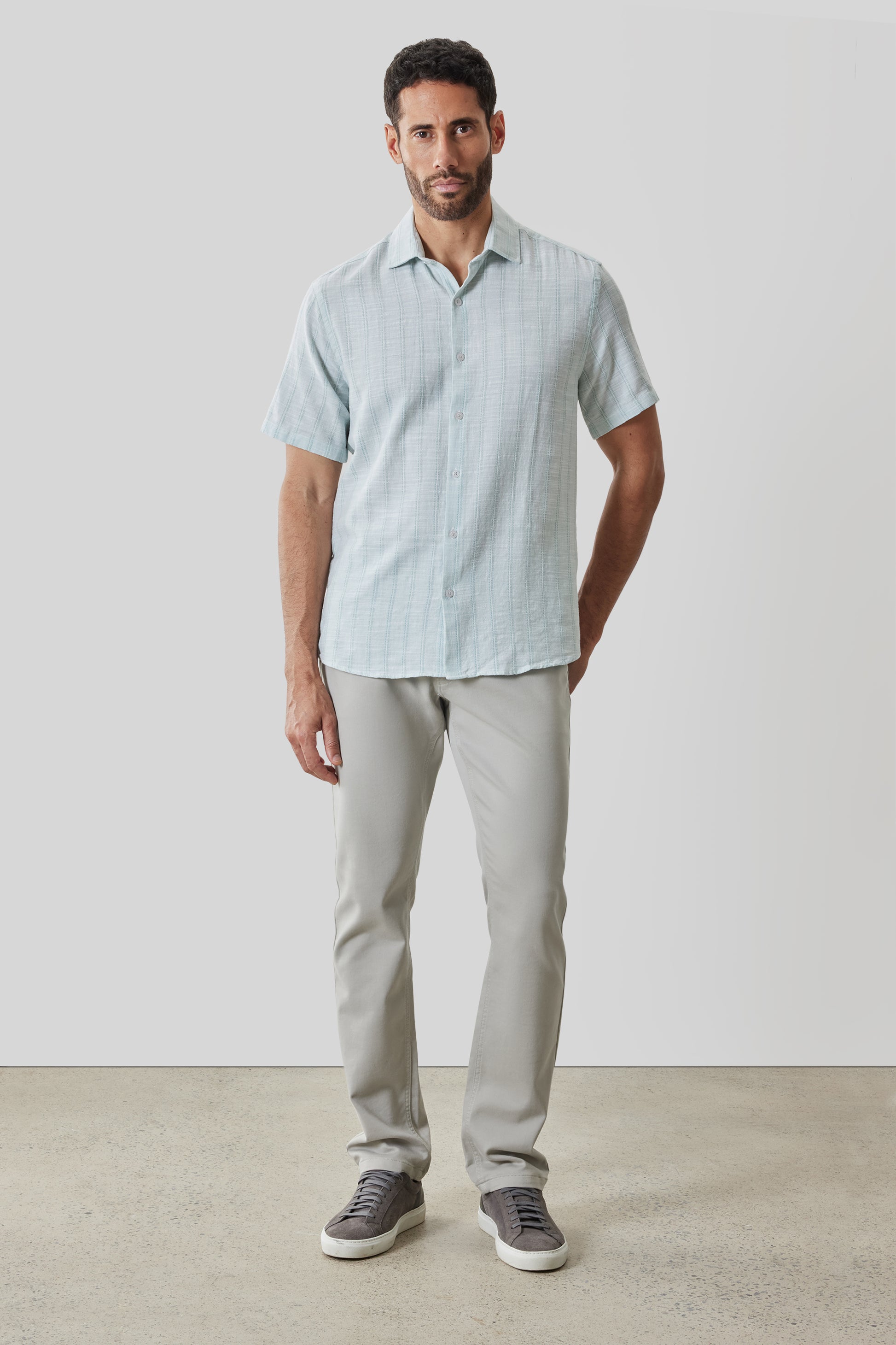 Man wearing light blue short-sleeve button-up shirt with grid pattern and beige pants.