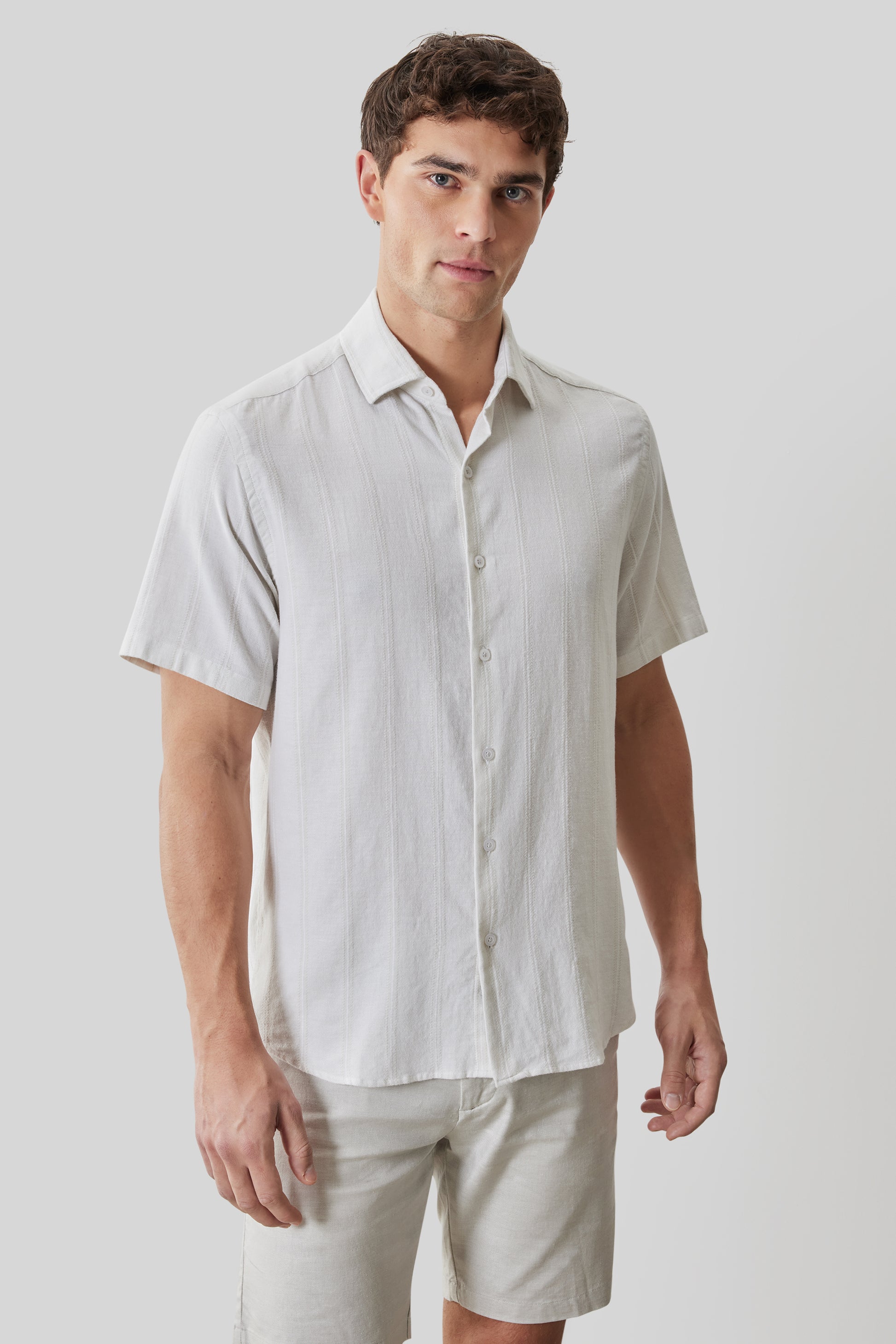 White linen short-sleeve button-up shirt with spread collar on model wearing light pants.