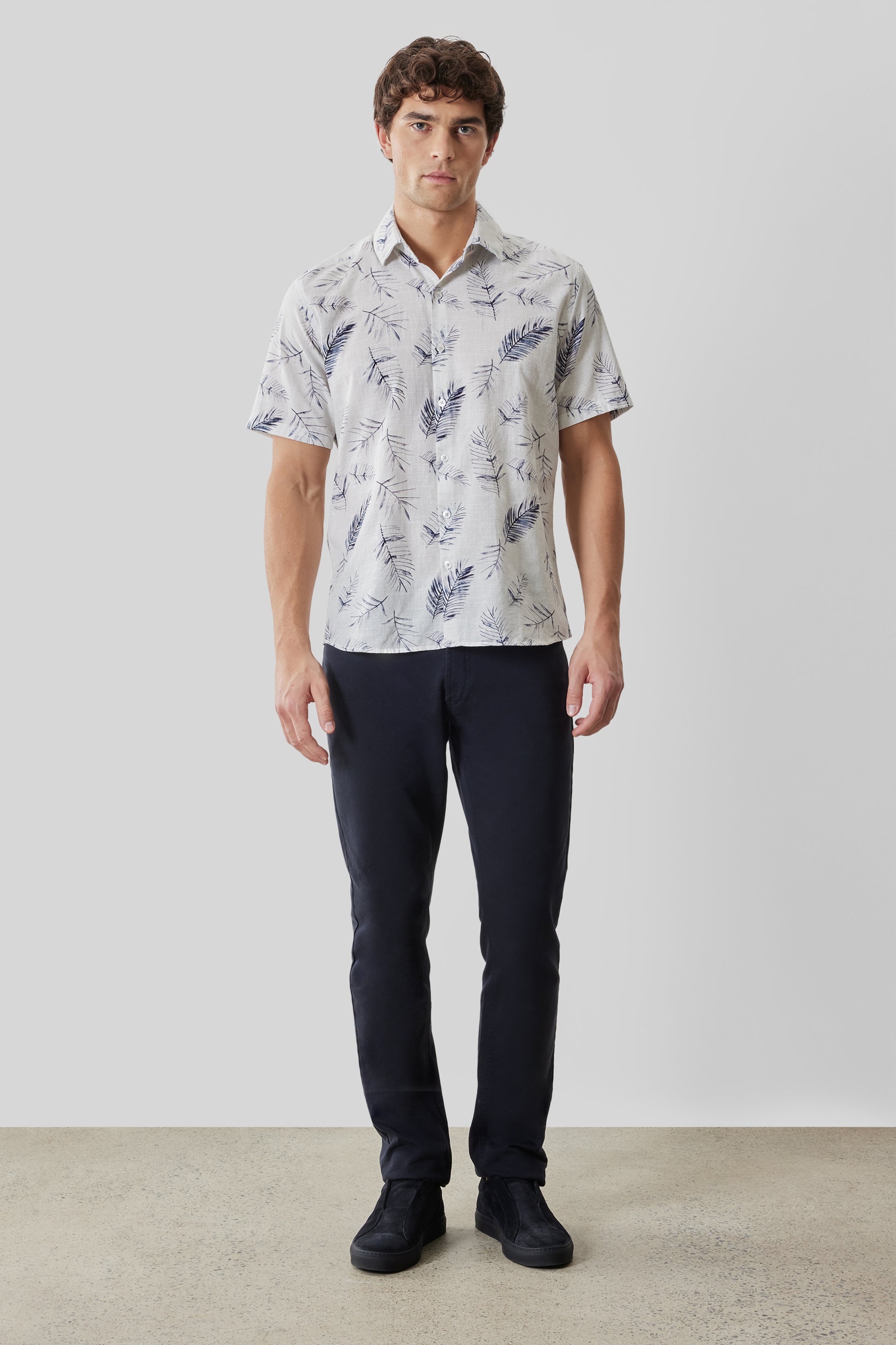 Man wearing cream short-sleeve shirt with navy leaf print and dark navy trousers.