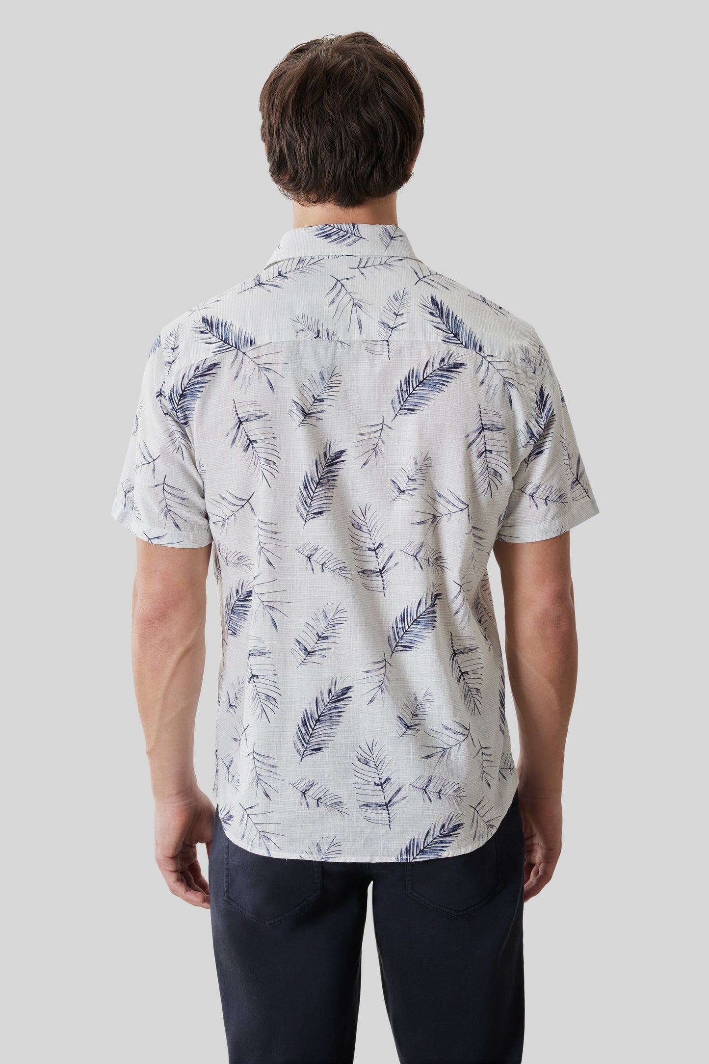 White short-sleeve shirt with navy feather pattern, shown from back on male model wearing dark pants.