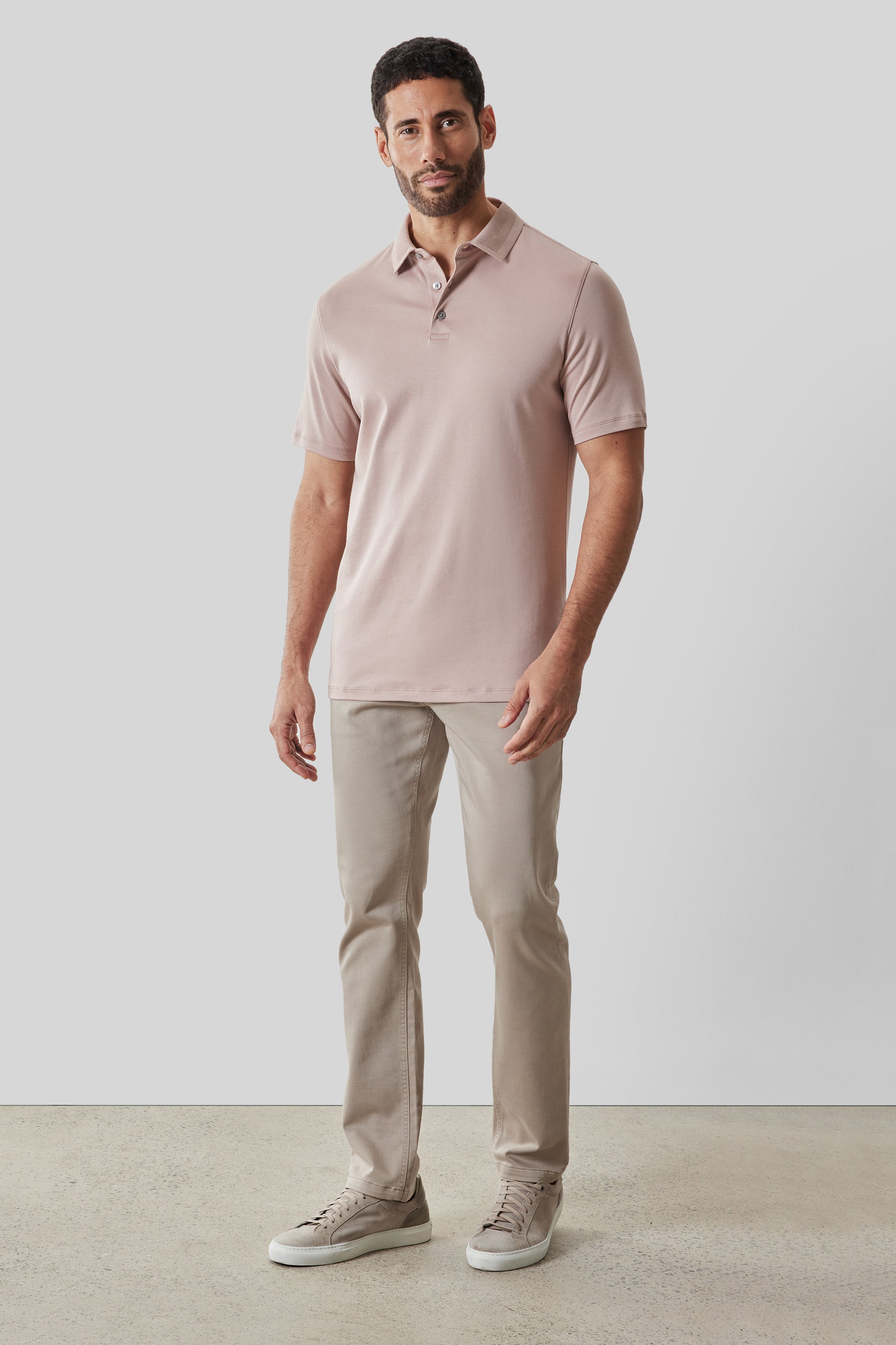 Man wearing a blush pink textured collar polo shirt with short sleeves and button front, paired with beige pants.
