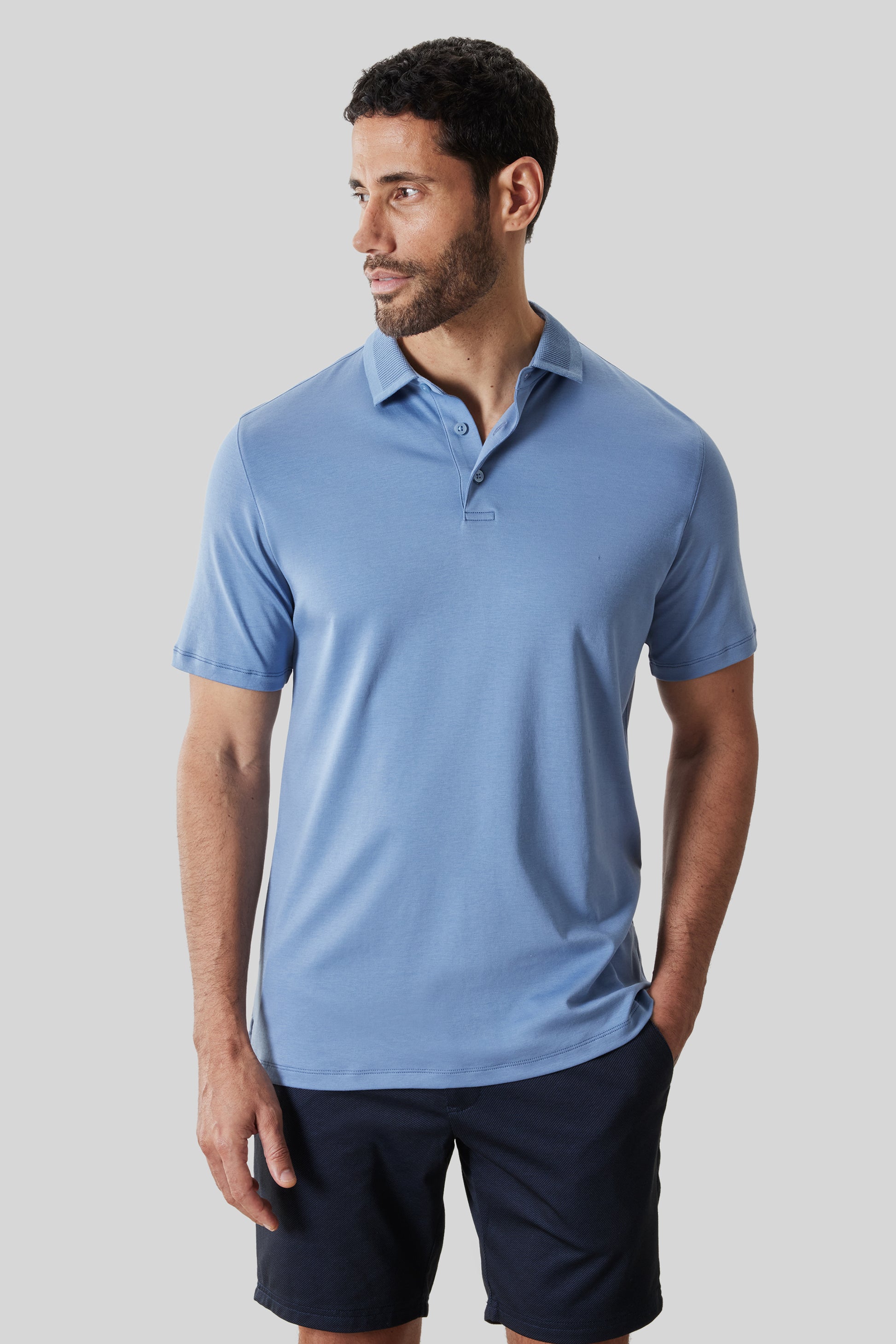Man wearing light blue short-sleeve polo shirt with textured collar and button placket, paired with navy shorts.