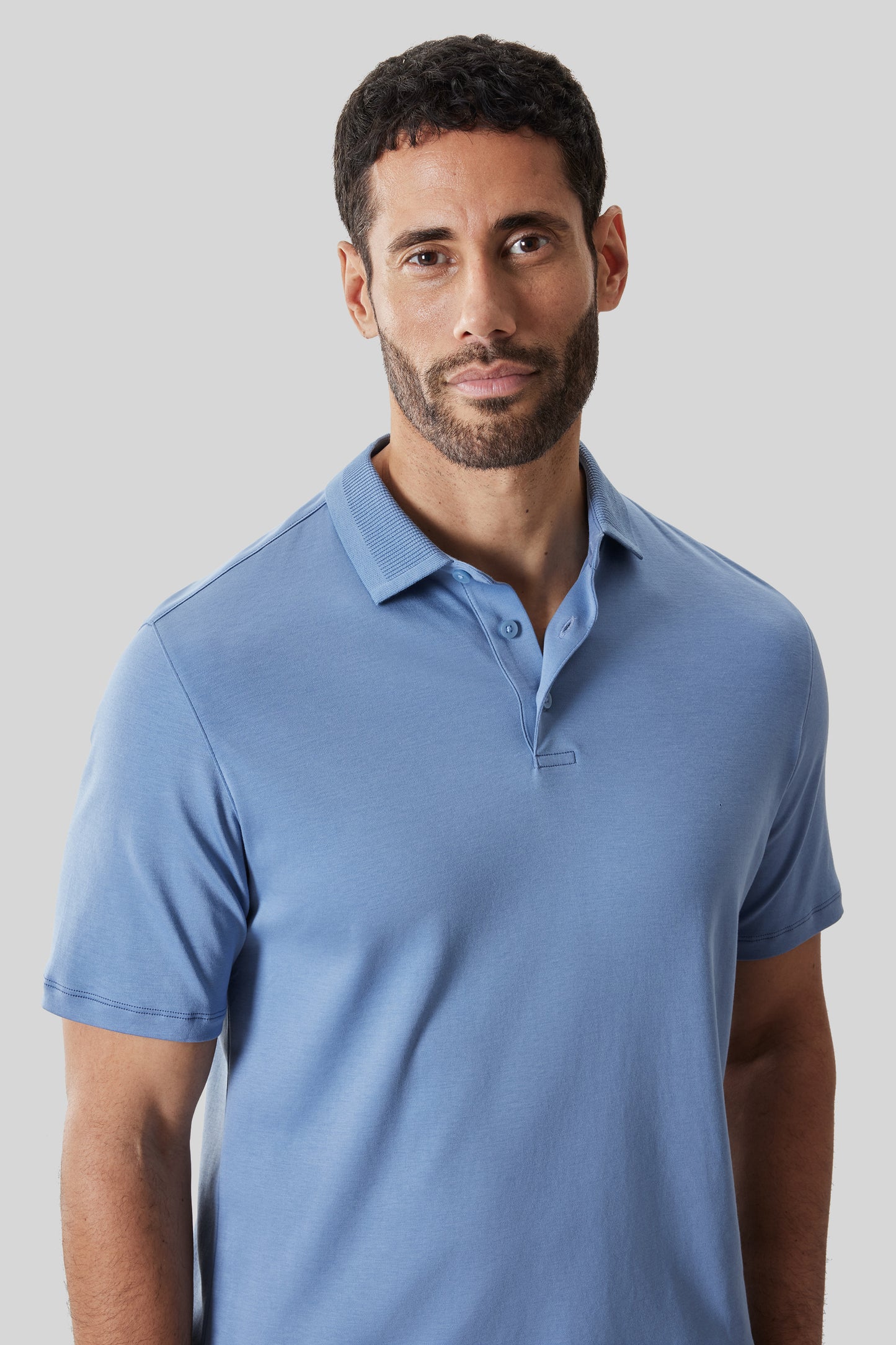 Man wearing light blue textured polo shirt with short sleeves and buttoned collar against neutral background.