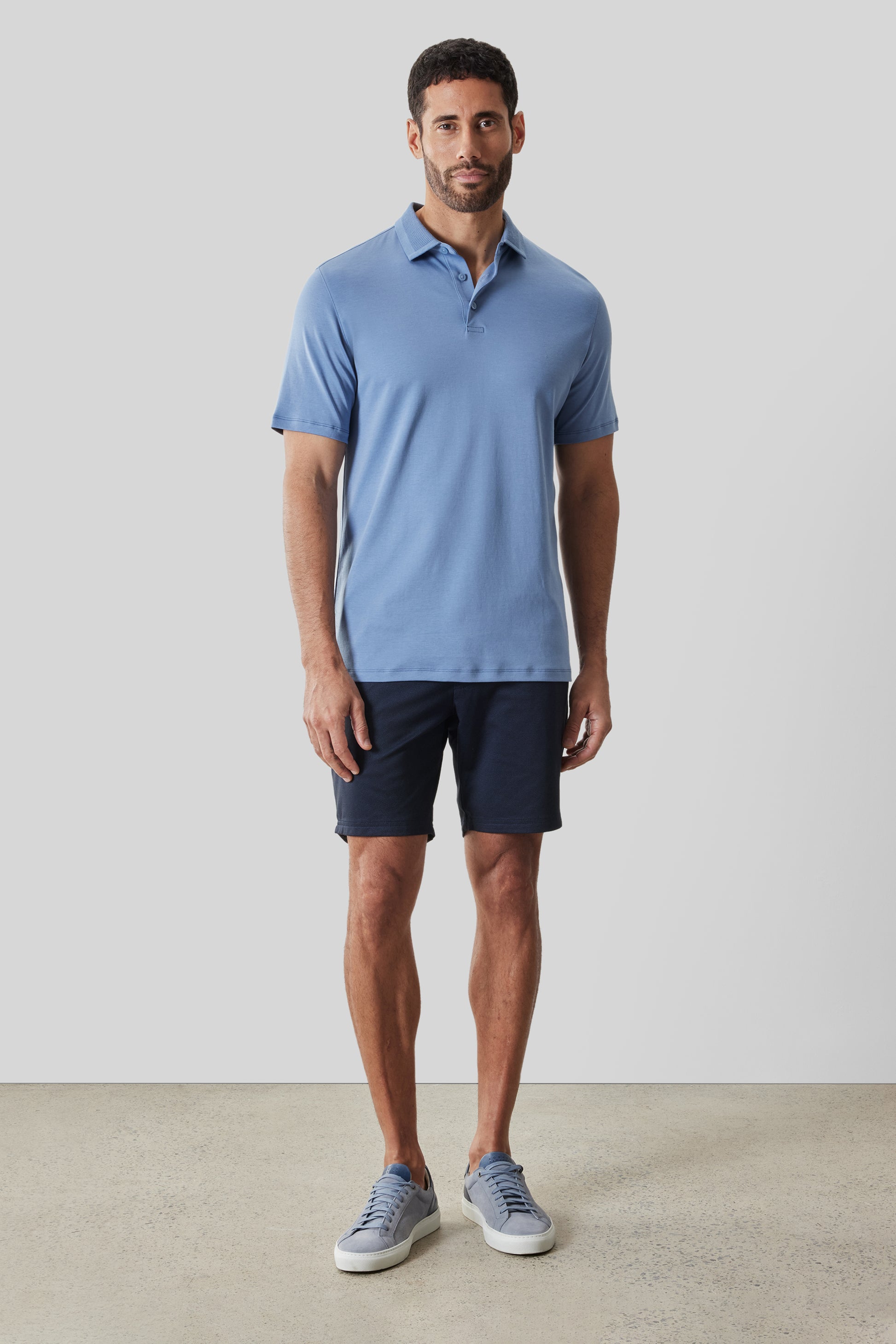 Man wearing light blue short-sleeve polo shirt with textured collar and dark navy shorts.