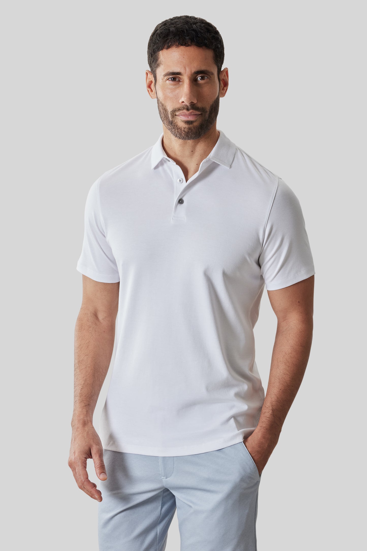 Man wearing white short-sleeve polo shirt with textured collar and button placket, paired with light blue pants.