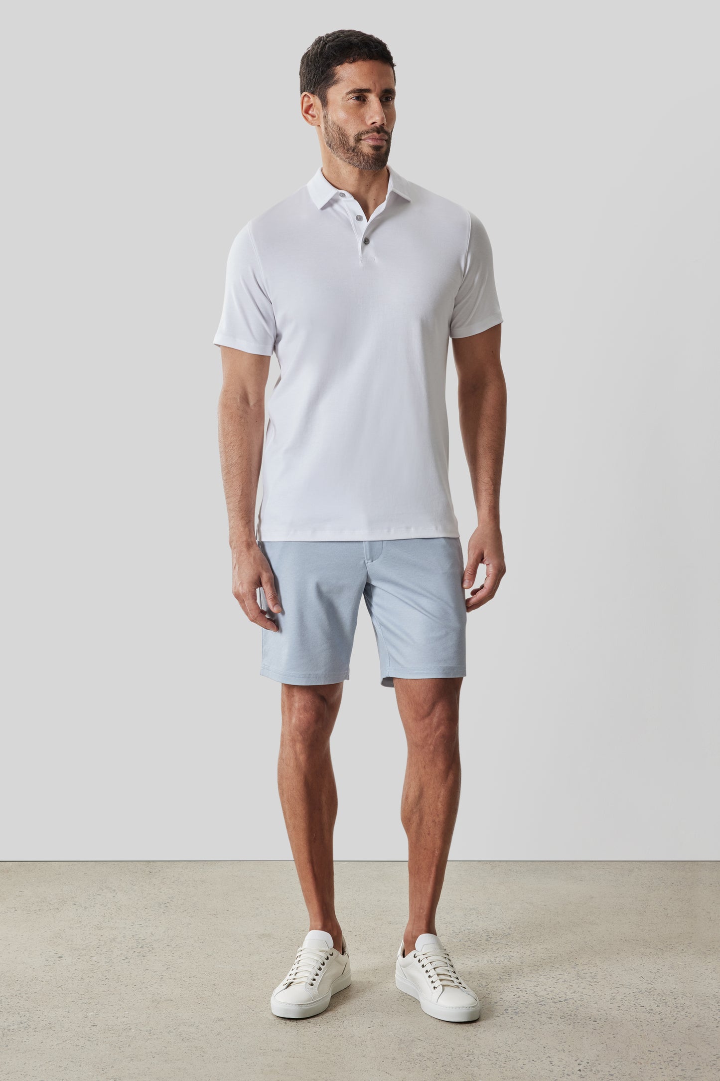 Man wearing white short-sleeve polo shirt with textured collar and light blue shorts, styled with white sneakers.
