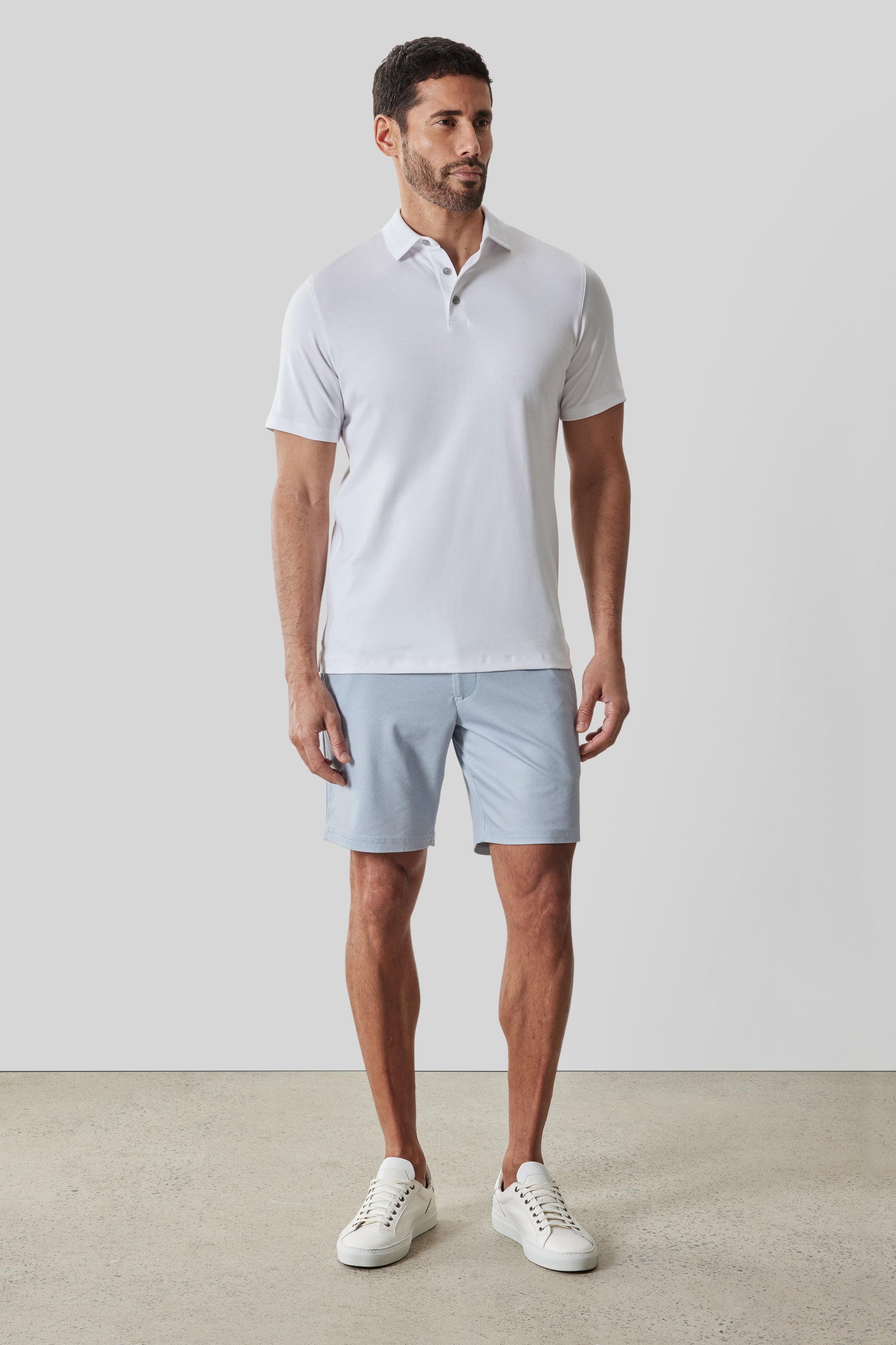Man wearing white short-sleeve polo shirt with textured collar and light blue shorts, styled with white sneakers.