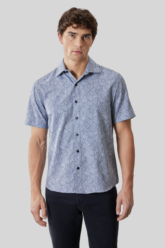 Man wearing light blue short-sleeve button-up shirt with dark geometric line pattern and dark navy pants.