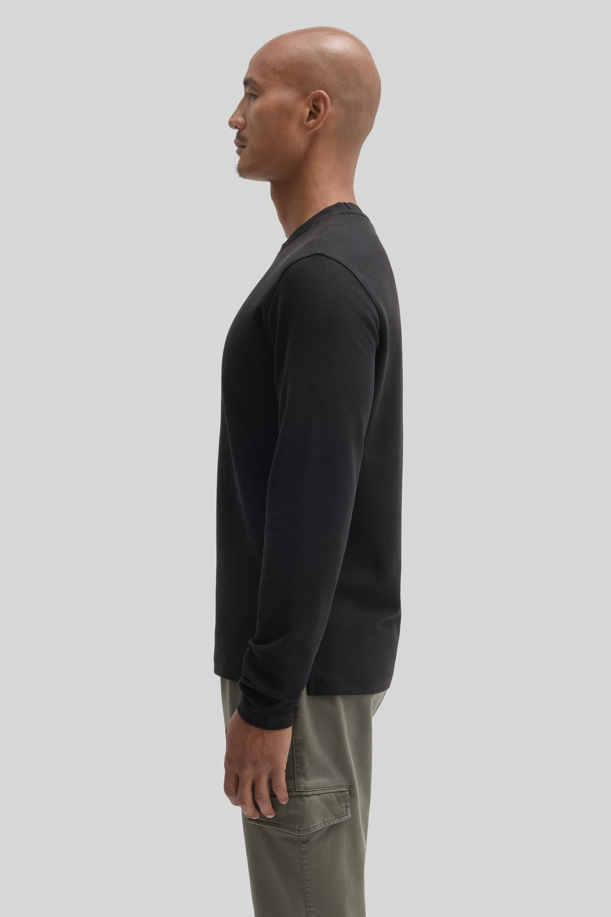 Man wearing black long-sleeve crew neckline top with olive cargo pants, shown in profile view.