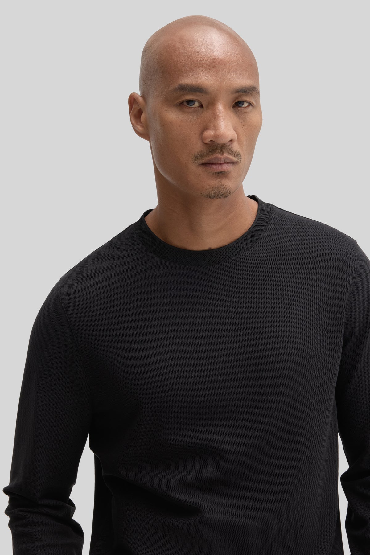 Man wearing black long sleeve crew neck shirt against neutral background.
