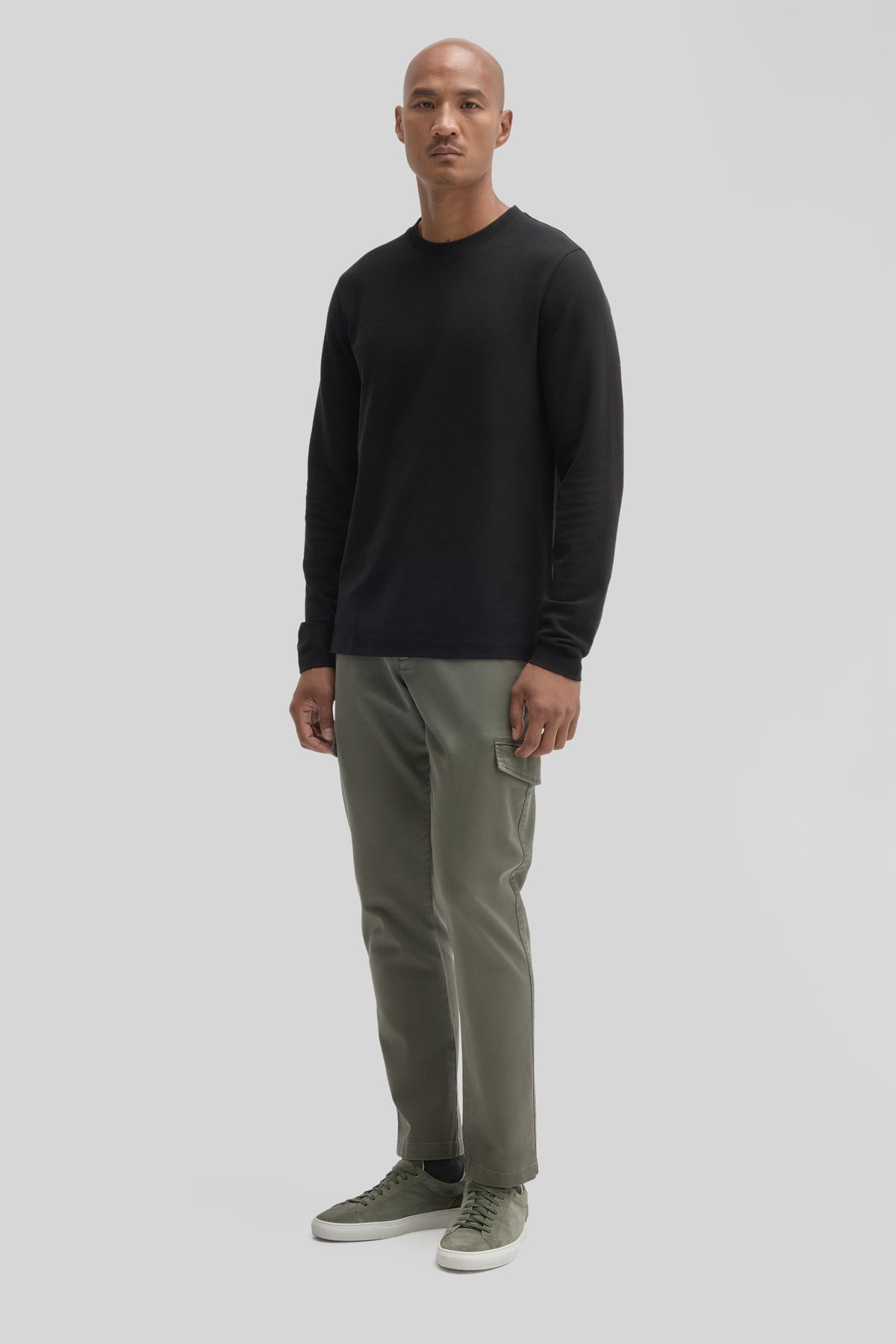 Man wearing black long sleeve crew neck shirt with khaki cargo pants and olive sneakers.