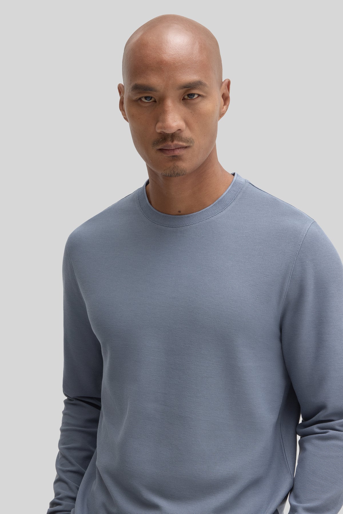 Man wearing a light blue long sleeve crew neck sweatshirt with textured fabric.