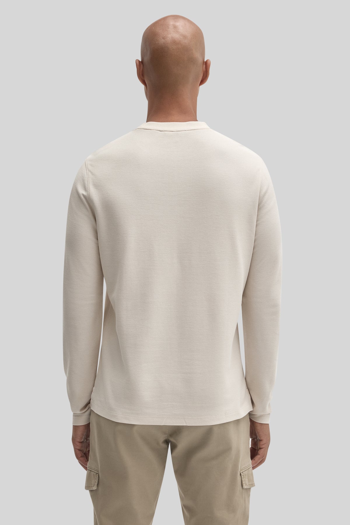 Man wearing cream-colored long sleeve crew neck shirt, shown from back view, paired with khaki cargo pants.