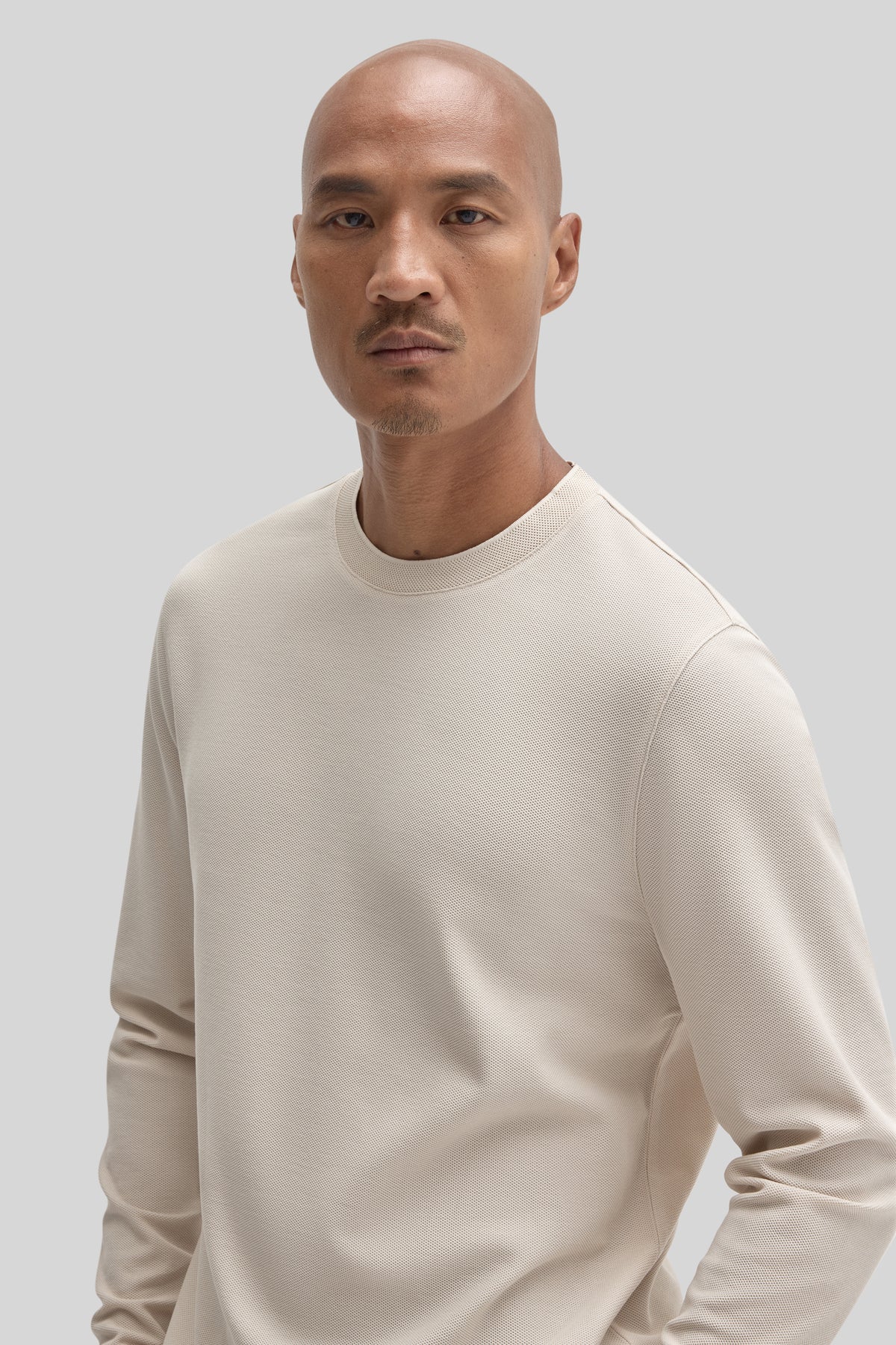 Beige long-sleeve crew neck sweatshirt with textured knit fabric worn by a man against a neutral background.