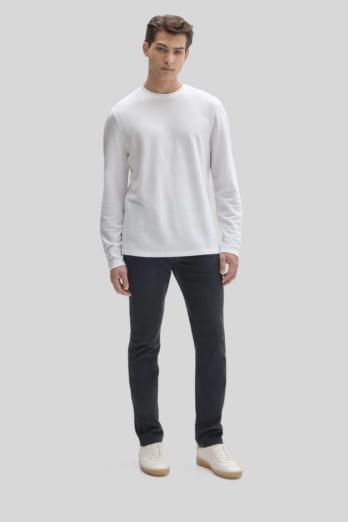 Man wearing white long sleeve crew neck shirt with black pants and cream sneakers.