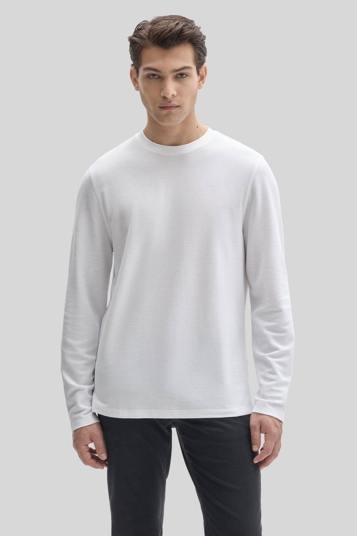 White long-sleeve crew neck shirt with ribbed cuffs worn with black pants.