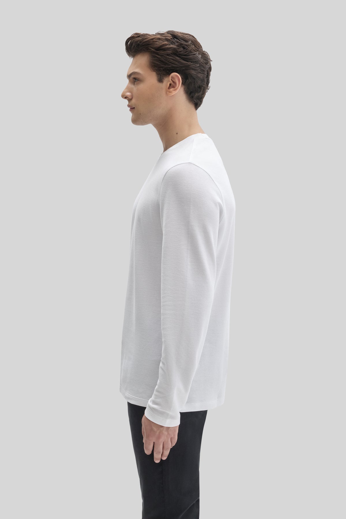 Man wearing white long-sleeve crew neck shirt with black pants, shown in profile view.