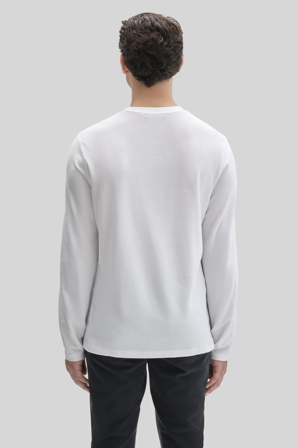 Man wearing white long-sleeve crew neck shirt with black pants, shown from back.