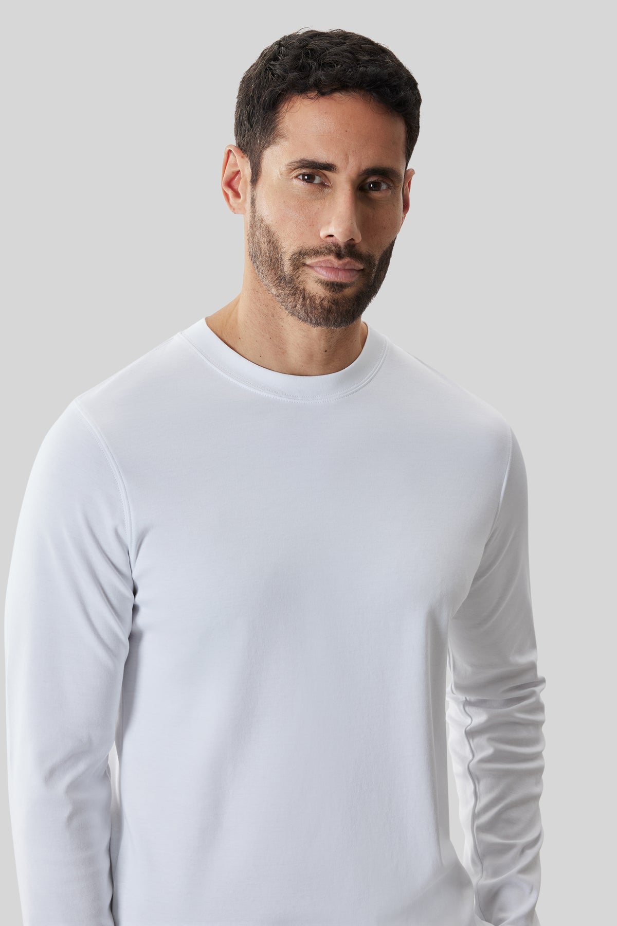 Man wearing white long-sleeve crew neck shirt against neutral background.
