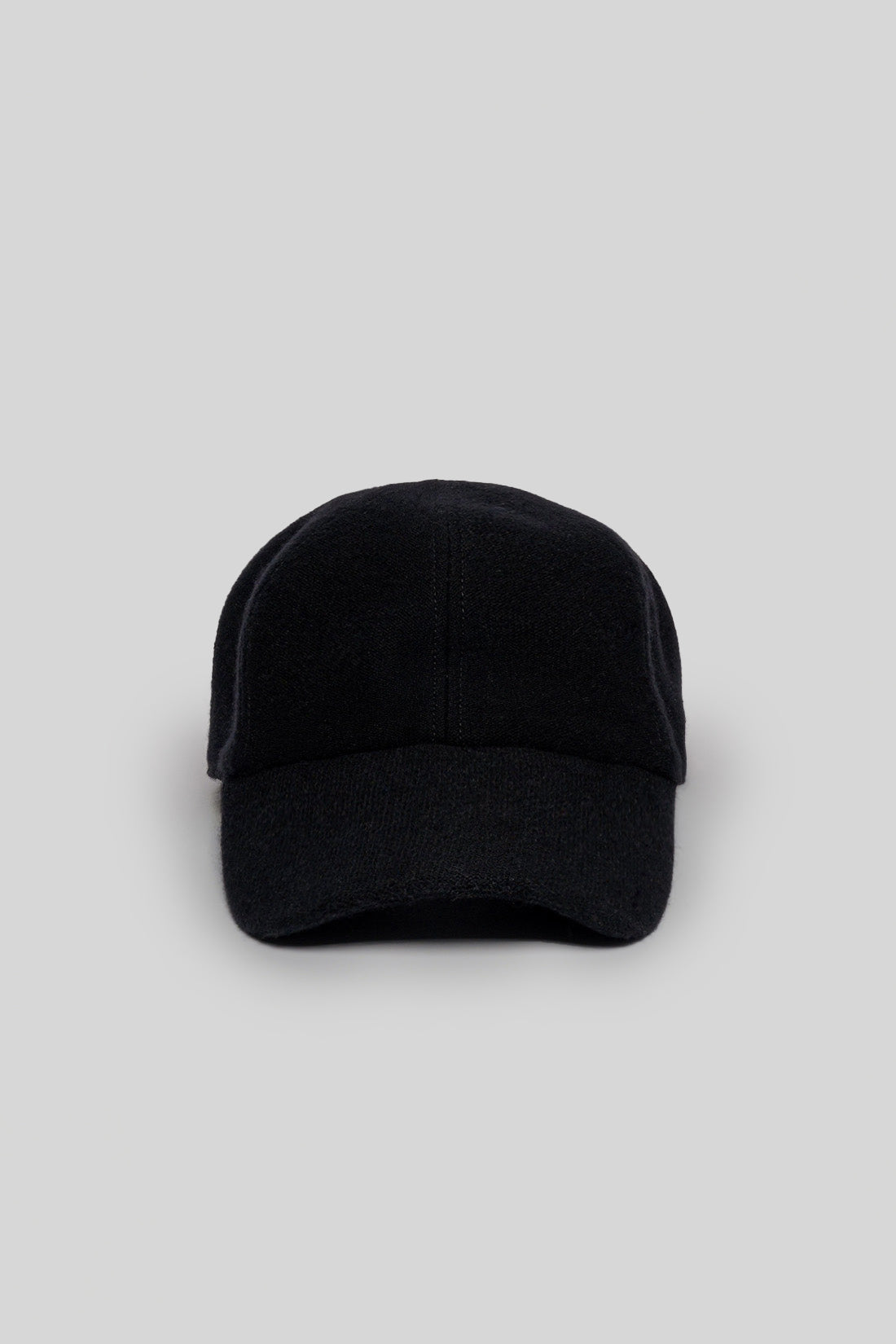 Black knit baseball cap with textured crown and brim against neutral background.