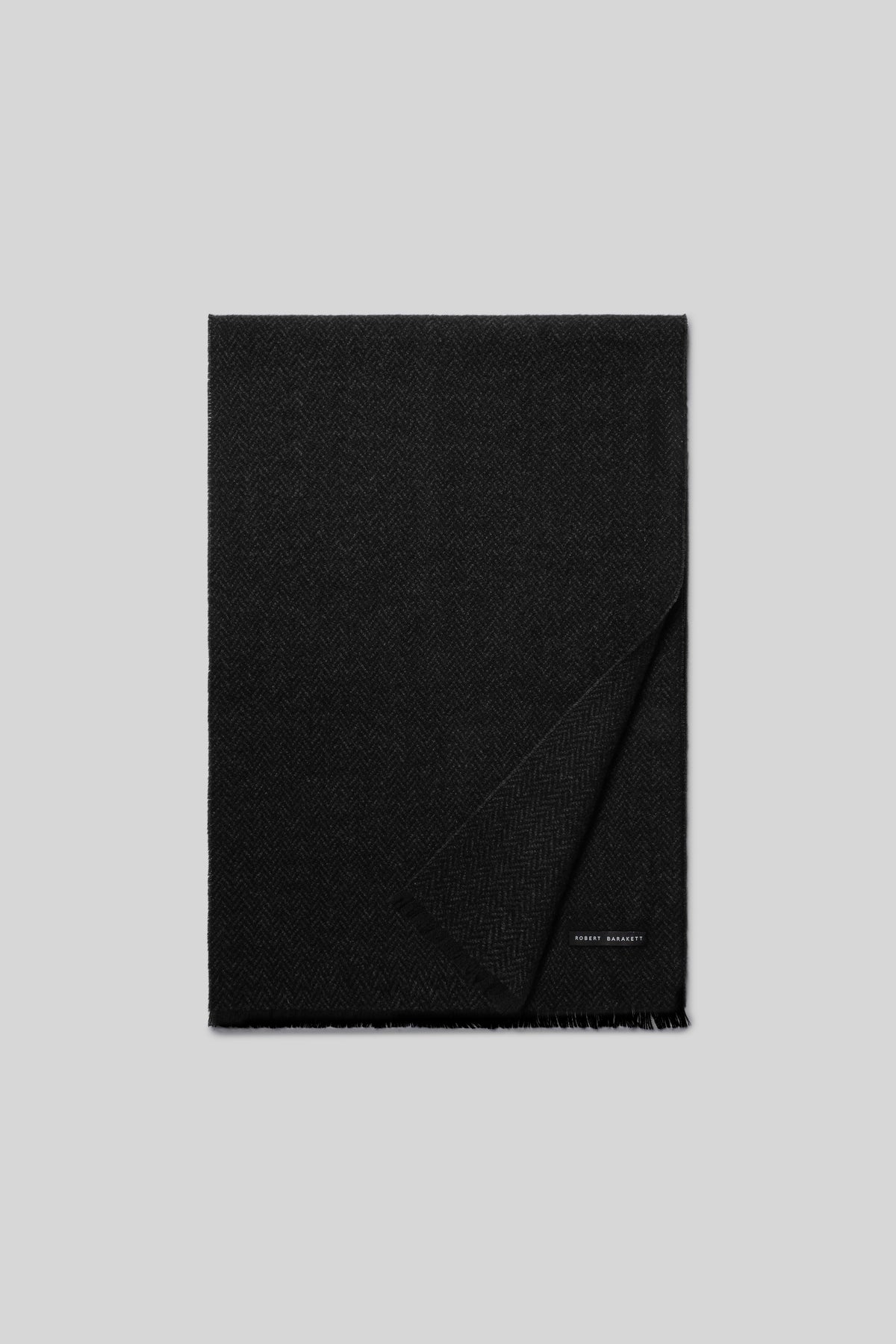 Black cashmere scarf with herringbone texture and fringed edges, partially folded.