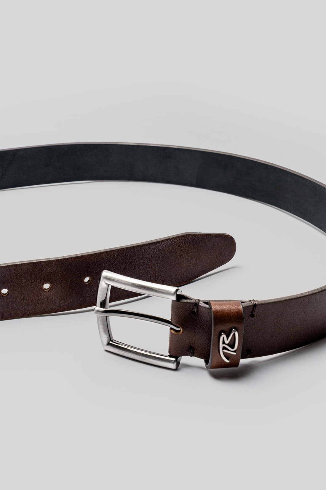 Brown leather belt with silver buckle and perforated holes, displayed with black belt coiled above.