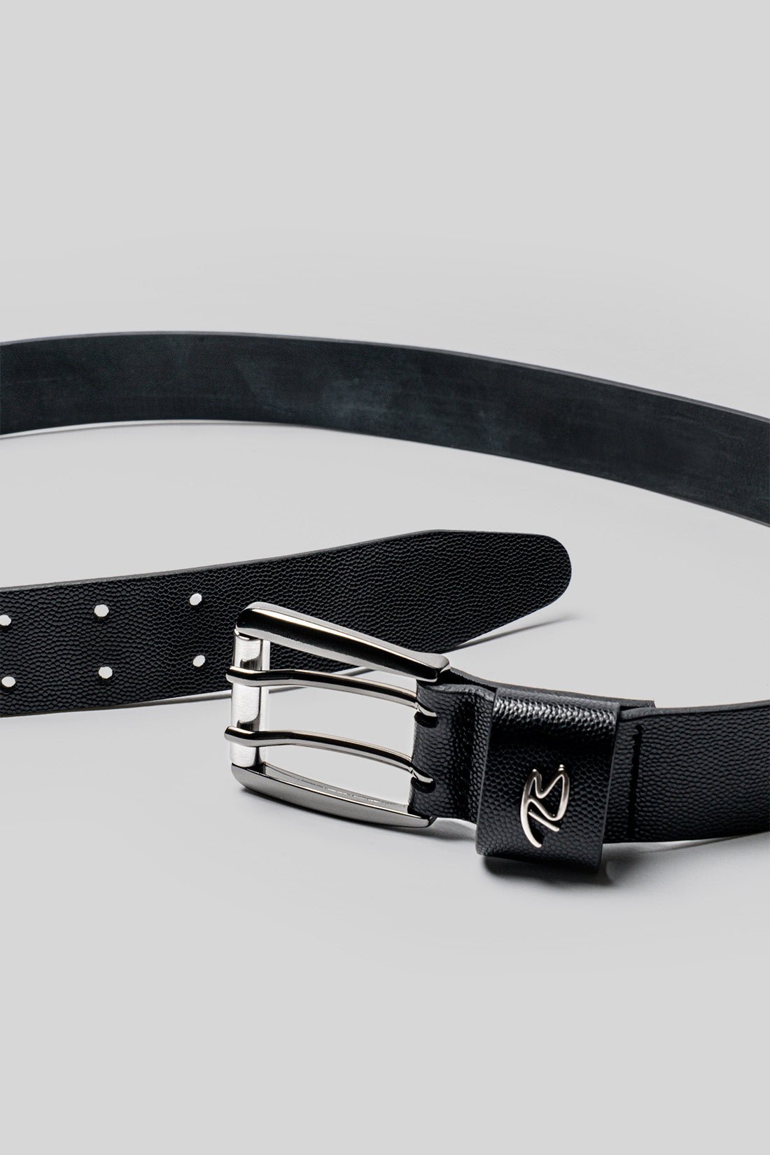 Black leather belt with textured strap, silver buckle with brand logo, and white adjustment holes.
