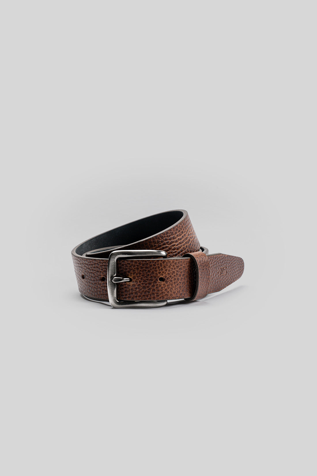 Brown pebbled leather belt with silver buckle and black underside, coiled on gray background.