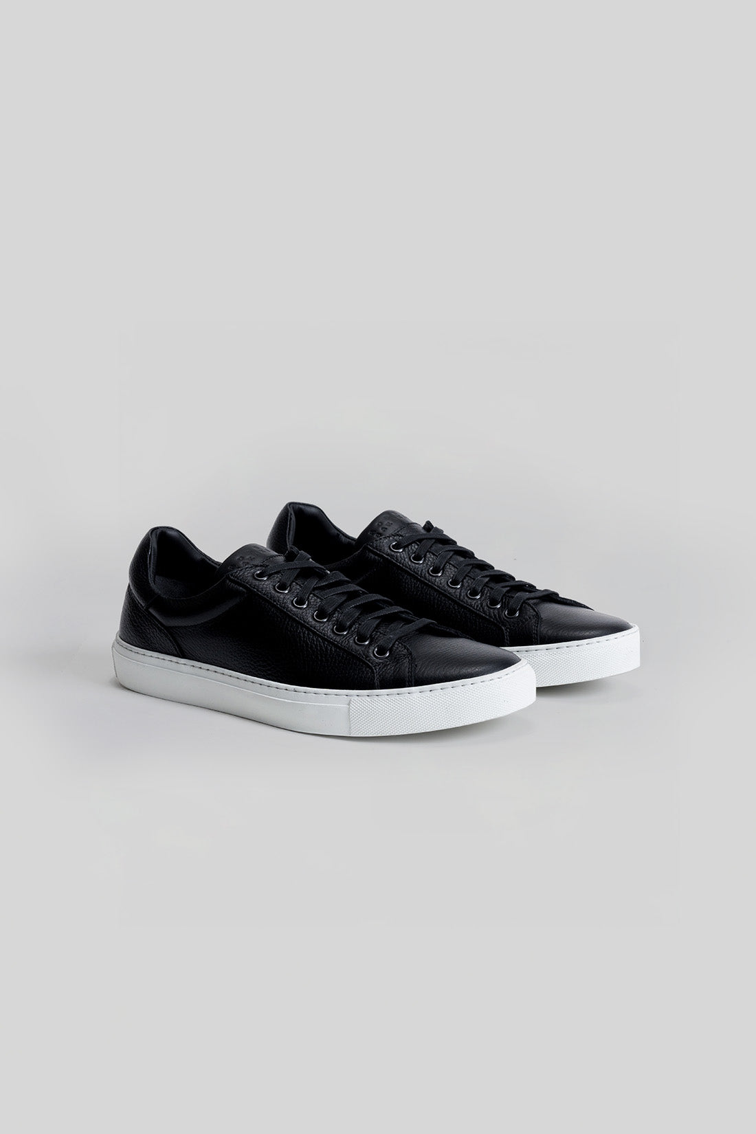 Black leather sneakers with white sole and black laces, shown as a pair from the side angle.
